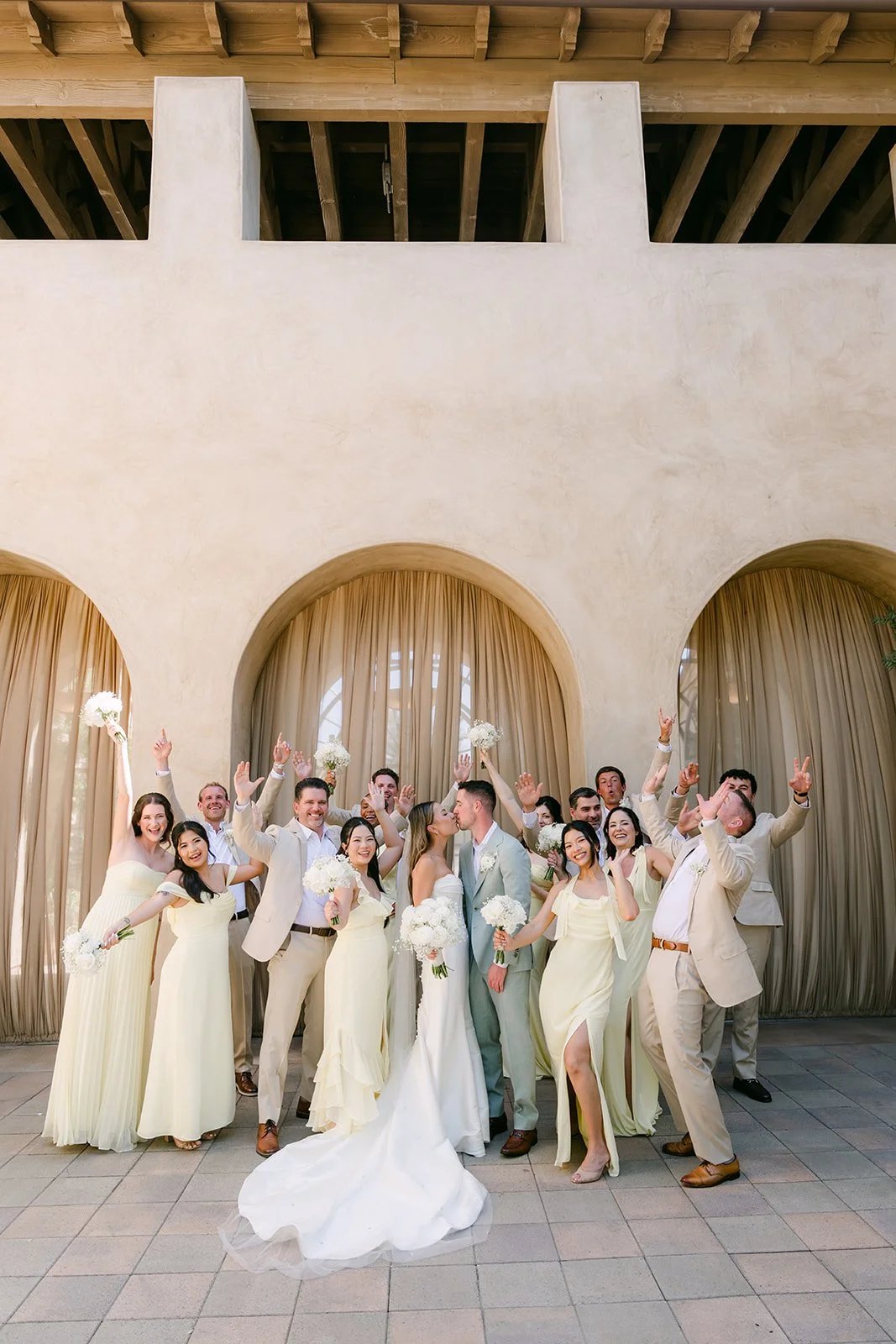 Wedding party raising bouquets in celebration under the terracotta archways