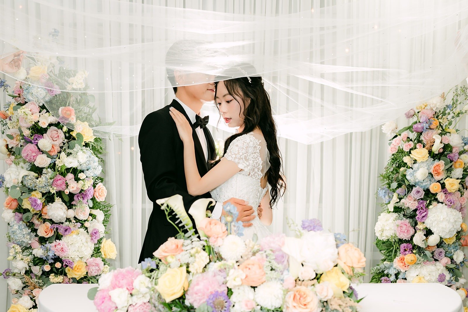 Jeannie and Eunsang sharing a kiss under her veil at the sweetheart table, photographed by One and Only Production