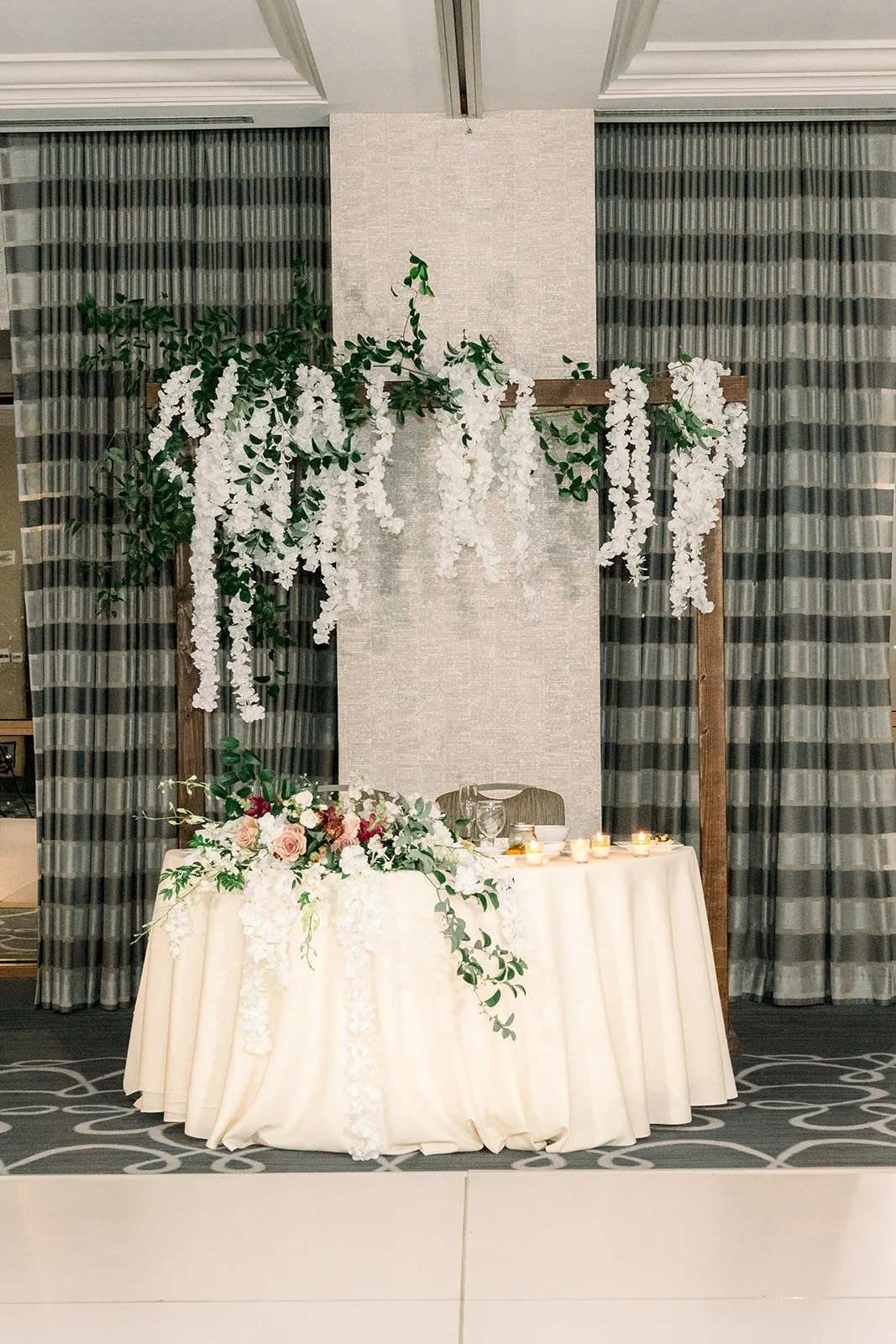 The sweetheart table with hanging white florals and a plaid backdrop, photographed by One and Only Production