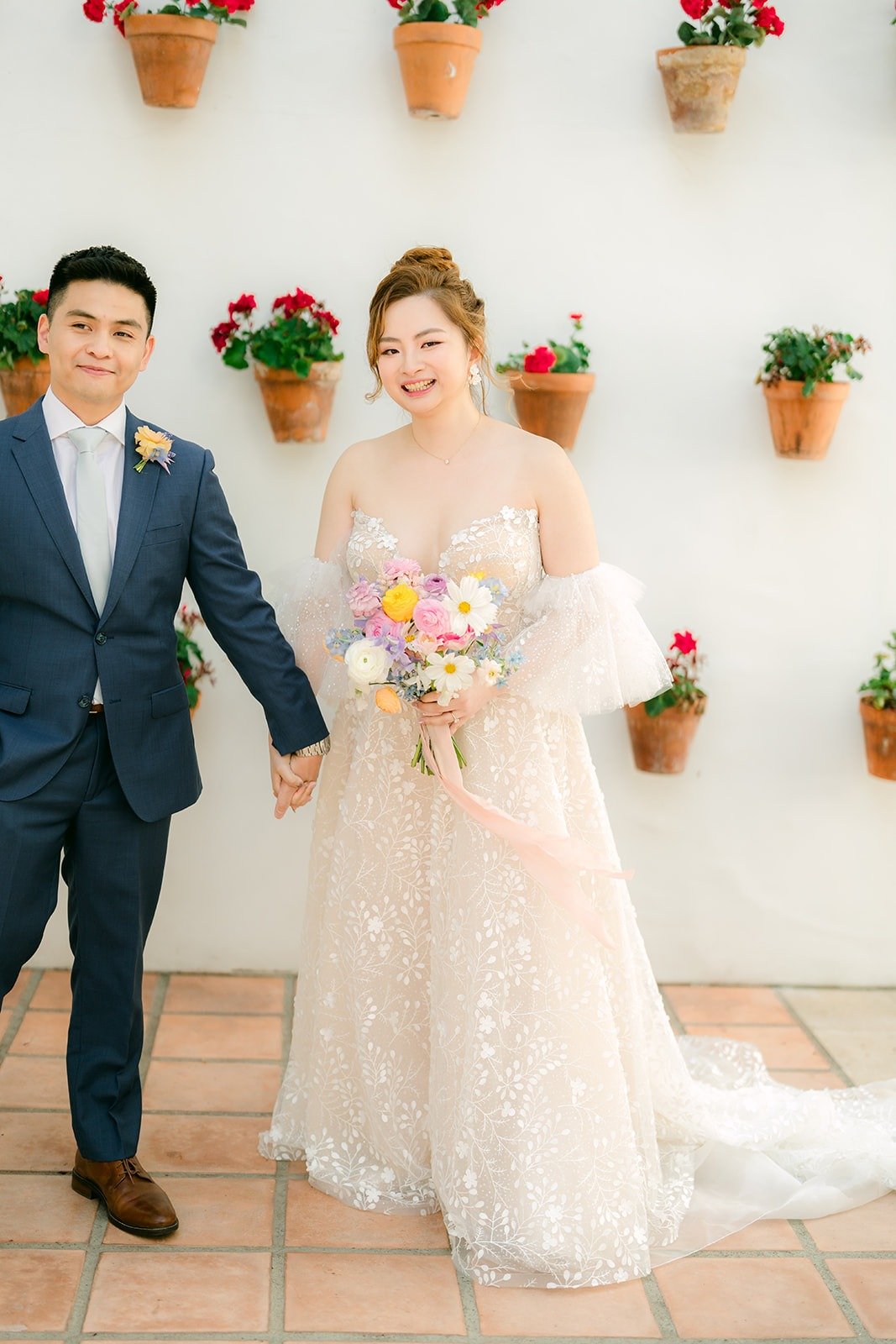 Joanna and Jerrick holding hands in front of the geranium wall