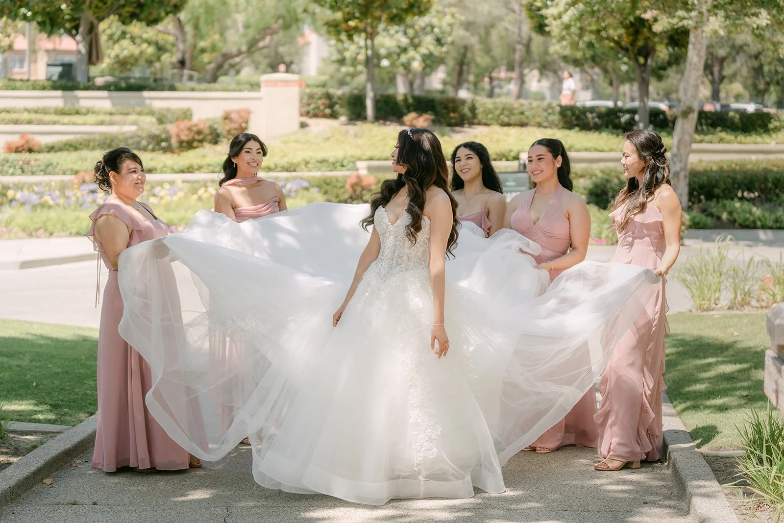 Sandra's bridesmaids in dusty pink carrying her train across the bridge.
