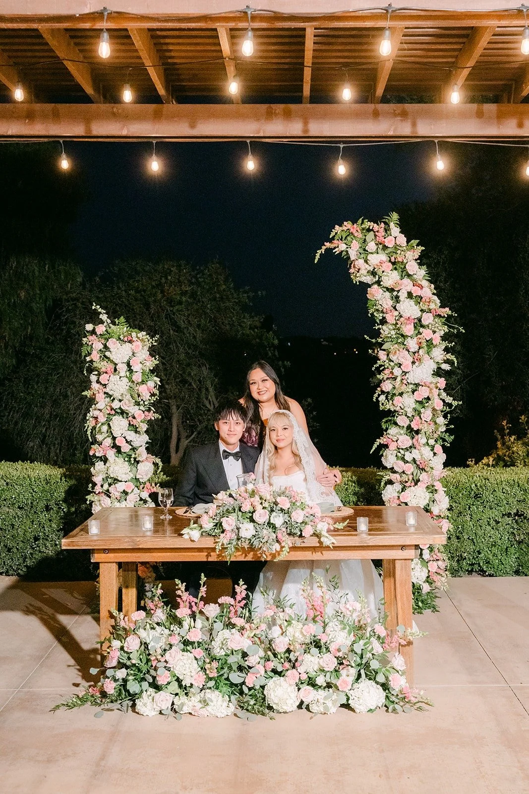 The floral sweetheart table glowing under the pergola lights