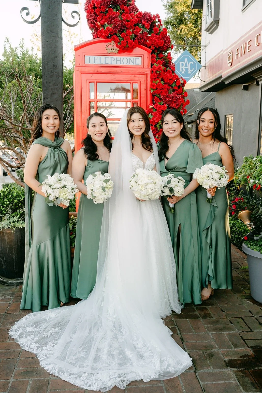Valerie with her bridesmaids in sage green by the red roses