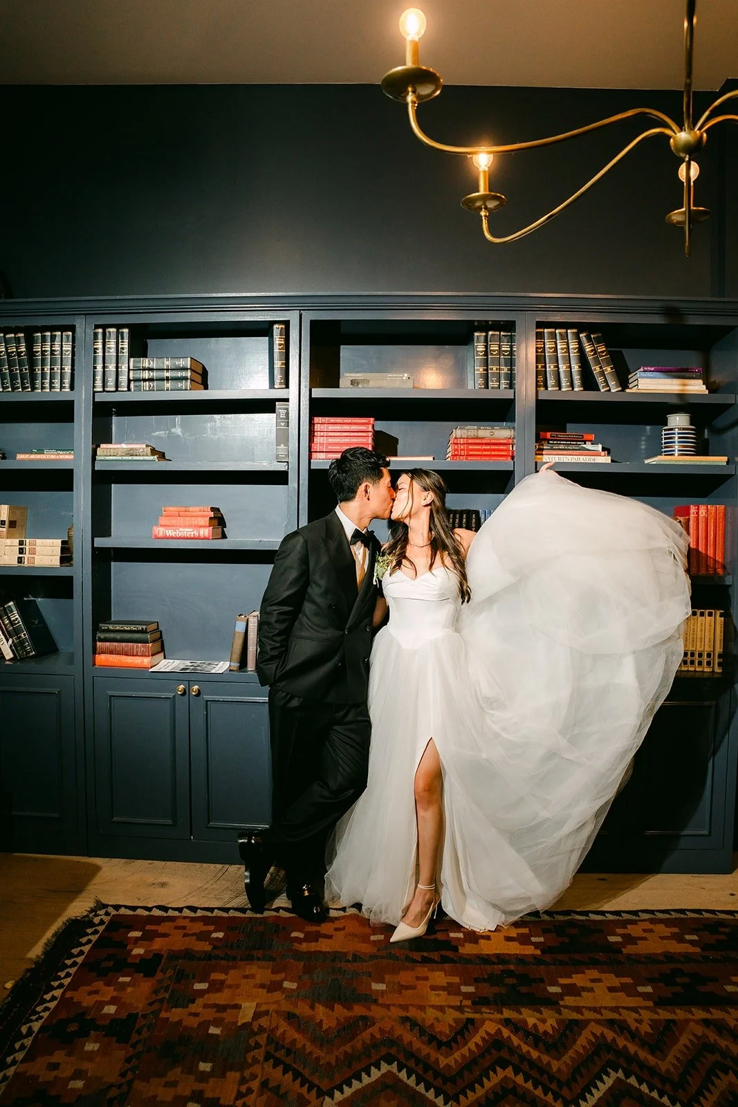 Jadee and Richard kissing by the bookshelves in the library suite, photographed by One and Only Production