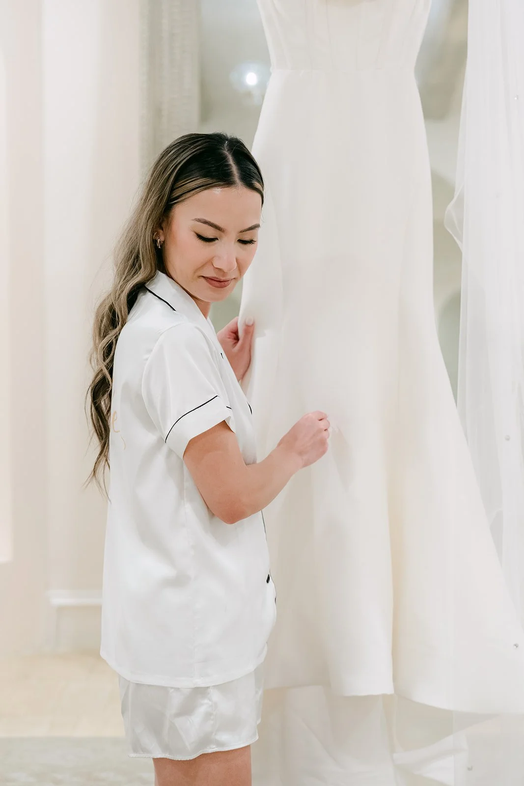 Bride touching her wedding gown as it hangs in the bright bridal suite
