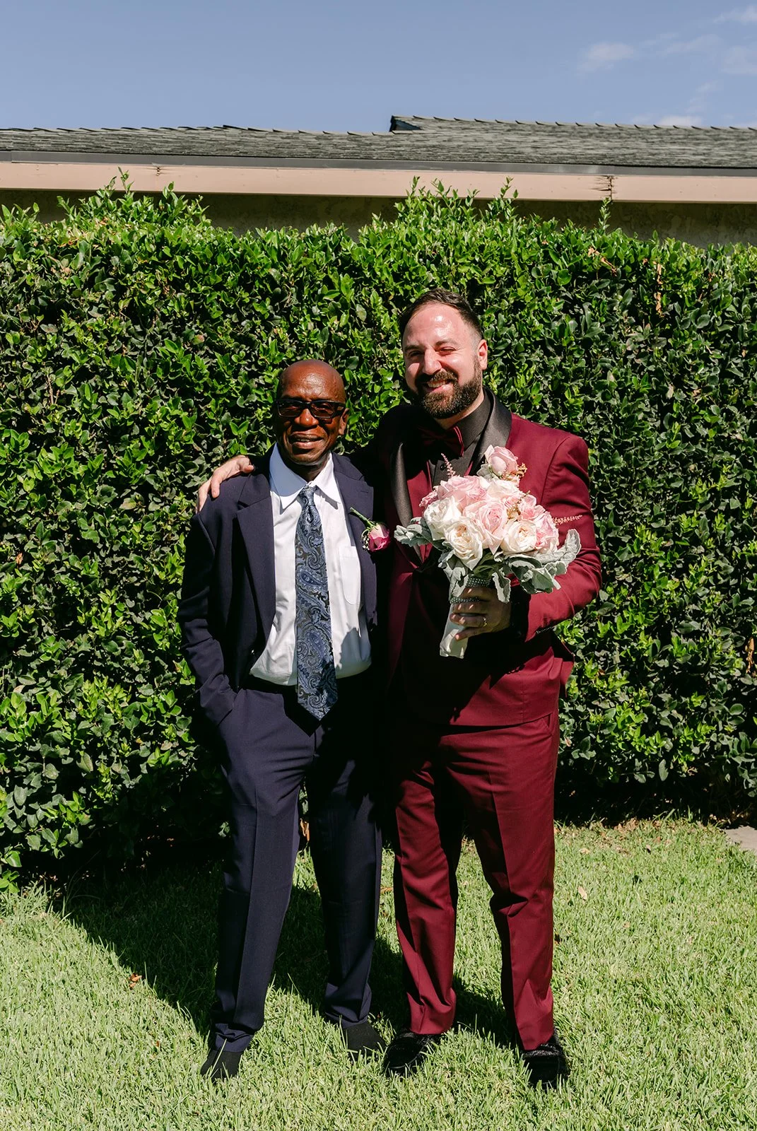 Ryan in his burgundy suit holding Vanessa's bouquet beside a friend.