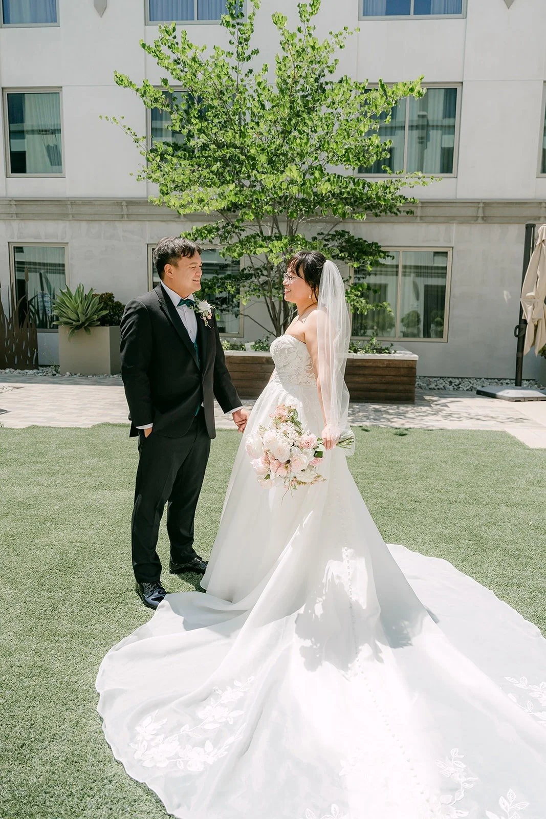 A wide portrait of Stella and James on the courtyard lawn surrounded by trees and the hotel walls