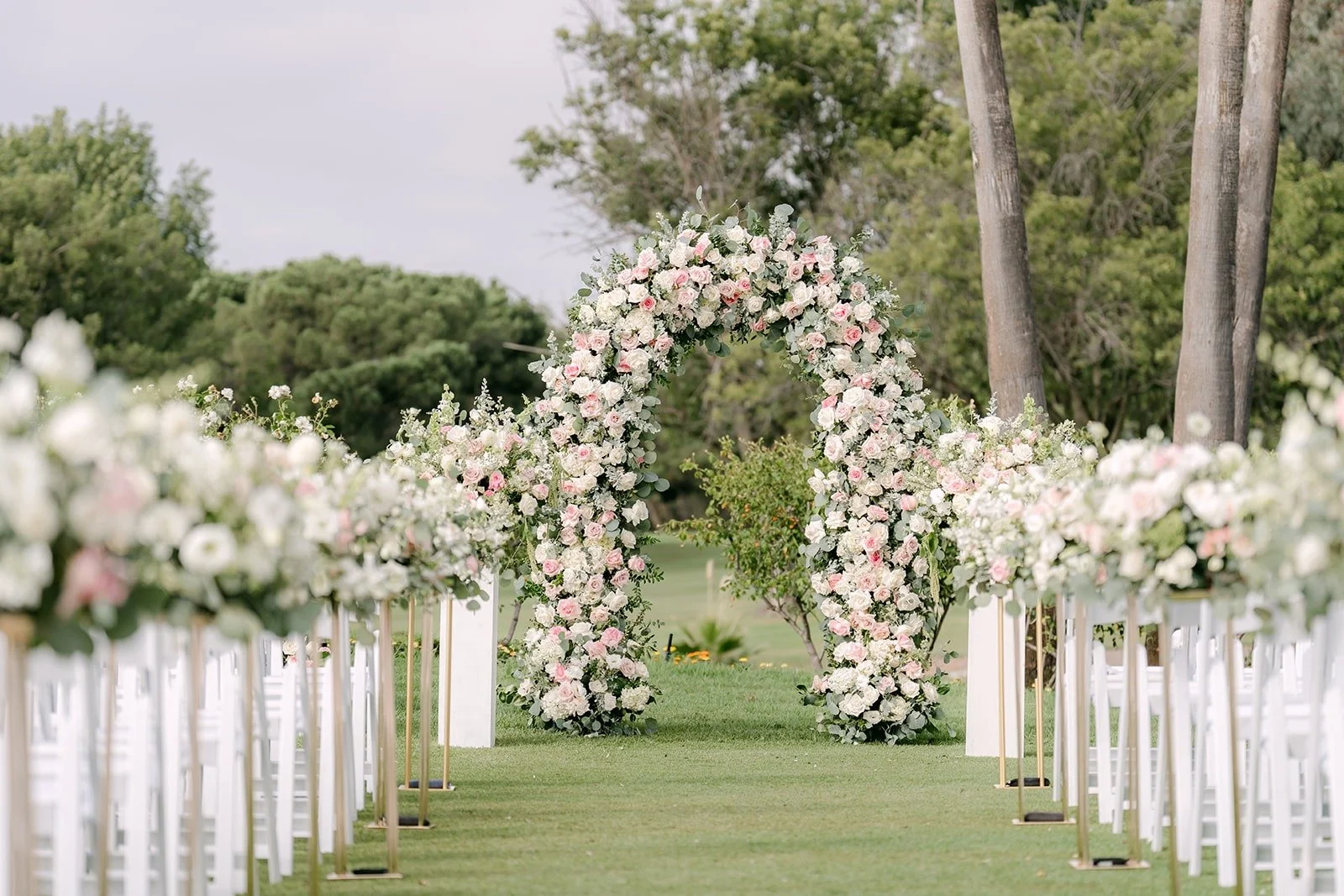 The ceremony aisle leading to a blush and ivory floral arch
