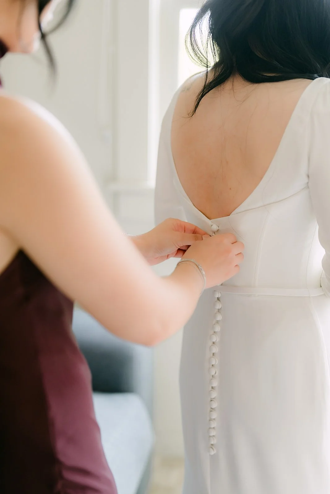 A bridesmaid fastening the buttons down the back of Denise's gown.