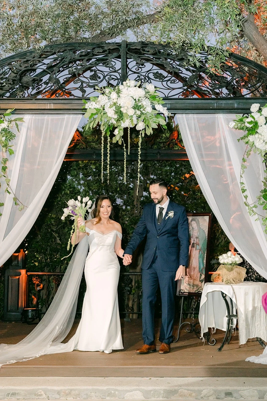 Mariana and Danny holding hands as newlyweds under the gazebo