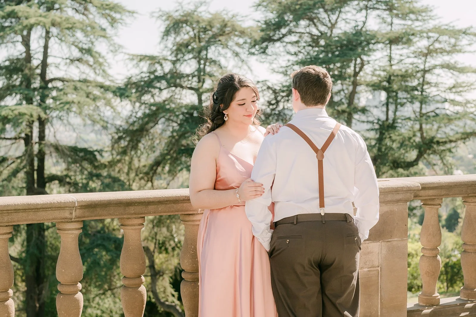 Saira and Matthew at the terrace balustrade surrounded by tall pines.