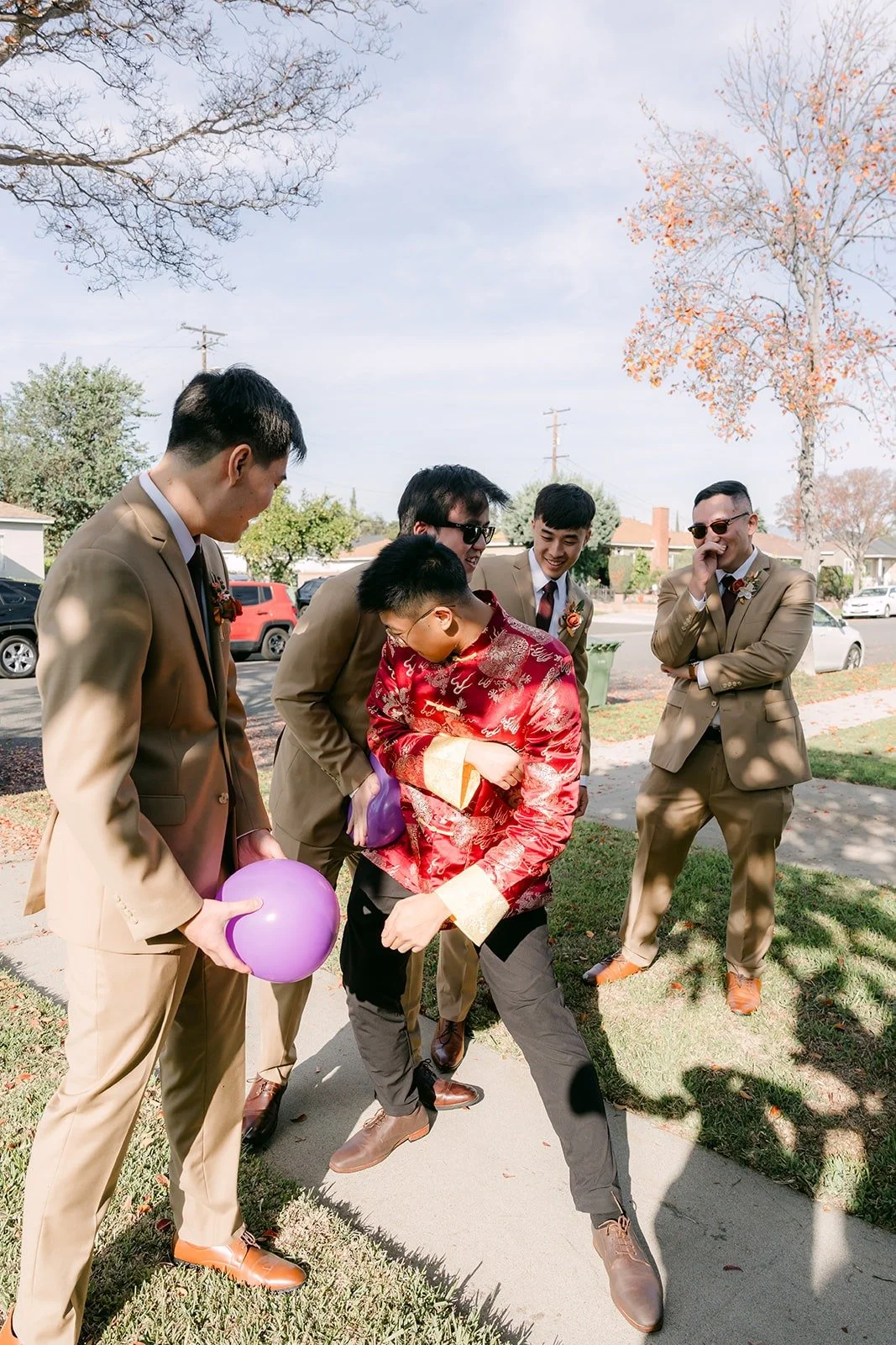 Groomsmen laughing through a balloon challenge on the front lawn