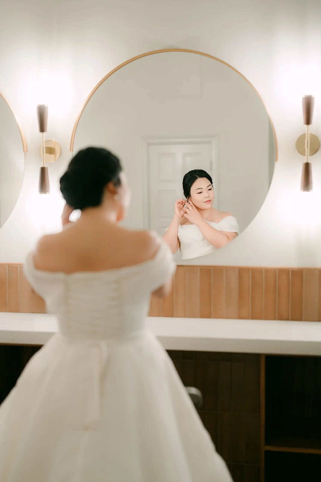 Chorok checking her look in a round mirror in a bright white suite
