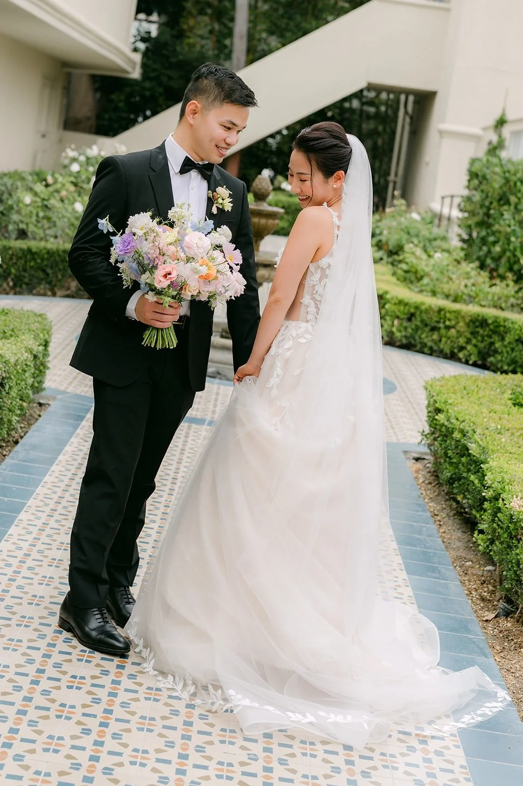 Kylie and Mario standing on the tiled garden path with her veil trailing behind