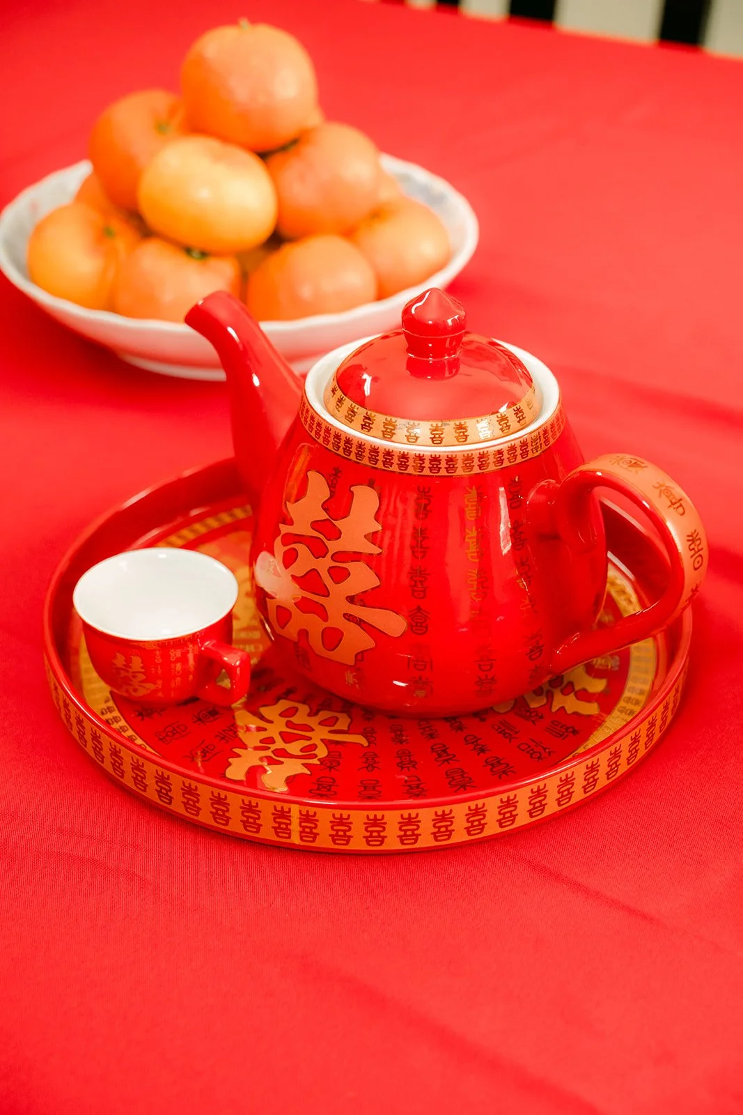 A red teapot and oranges on the tea tray.