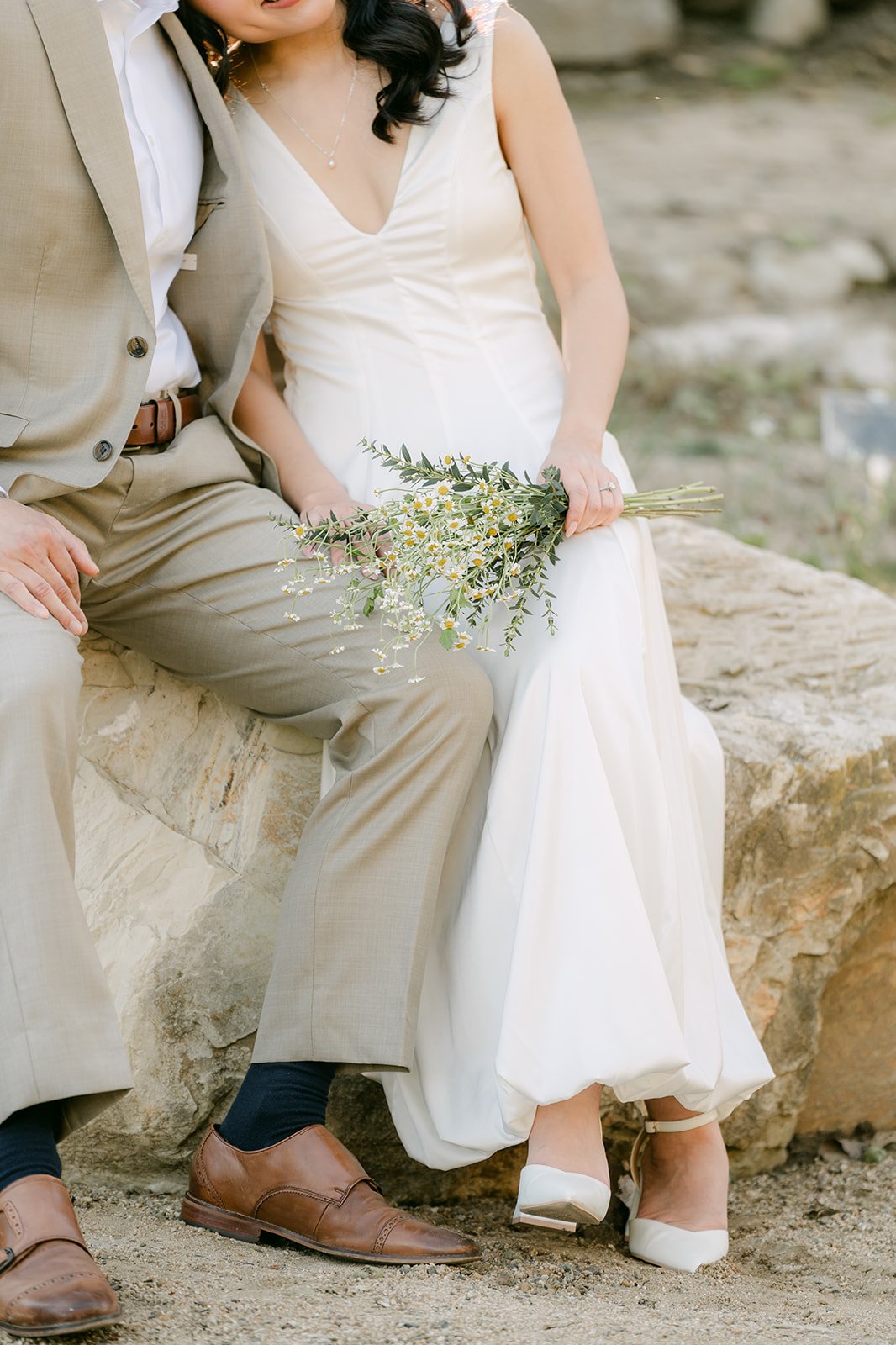 Detail of Kim and Vincent seated on a sandstone boulder with her bouquet in her lap.