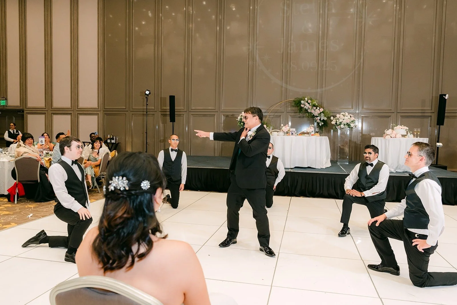 Groomsmen dropping to one knee during their dance as Stella watches