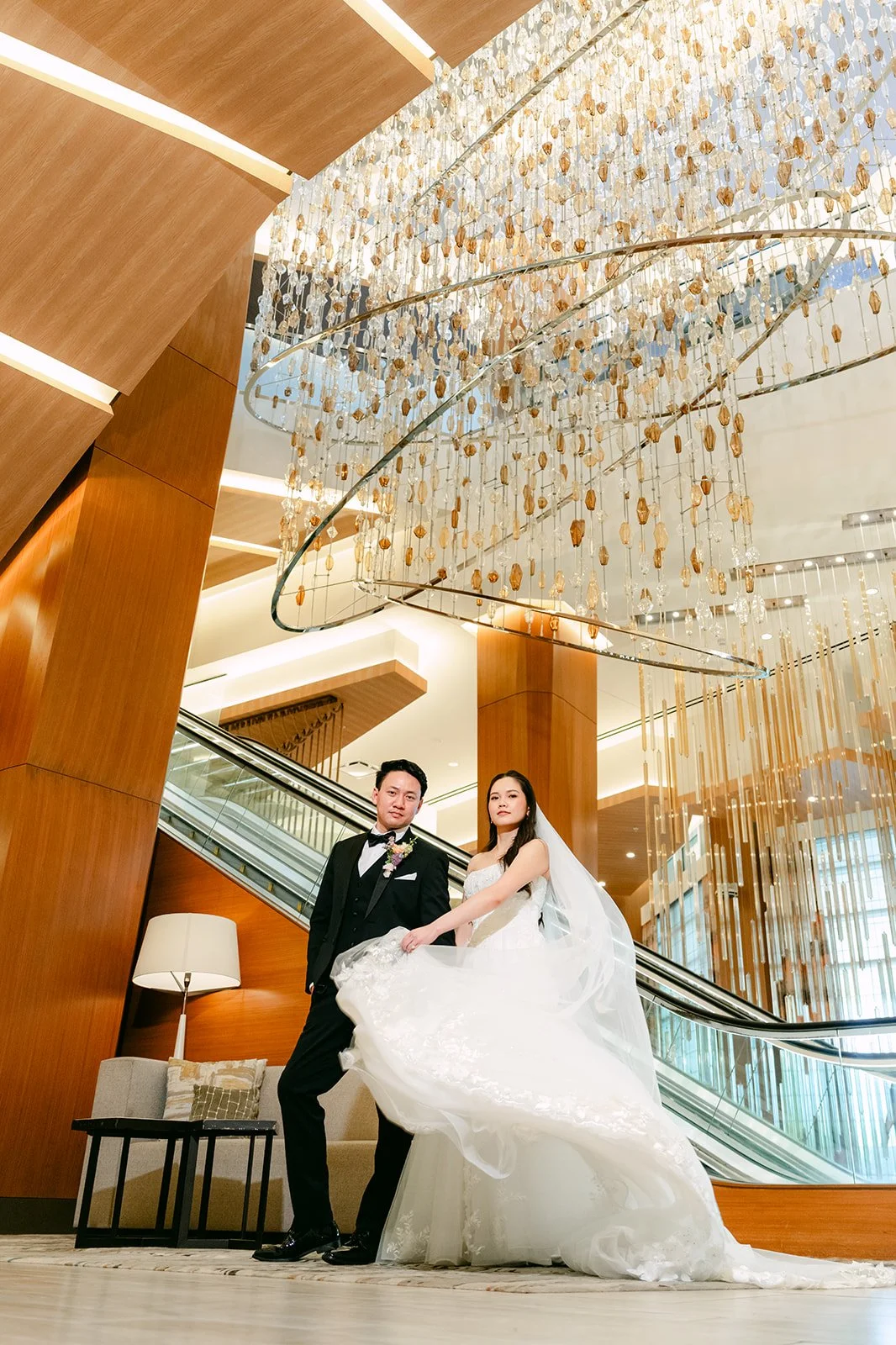 Groom holding the bride's gown on the lobby staircase landing