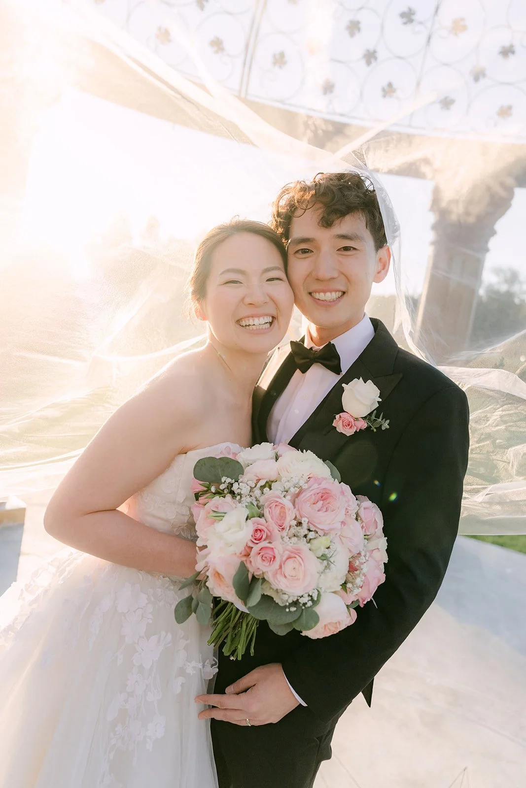 Couple laughing under the bride's flowing veil