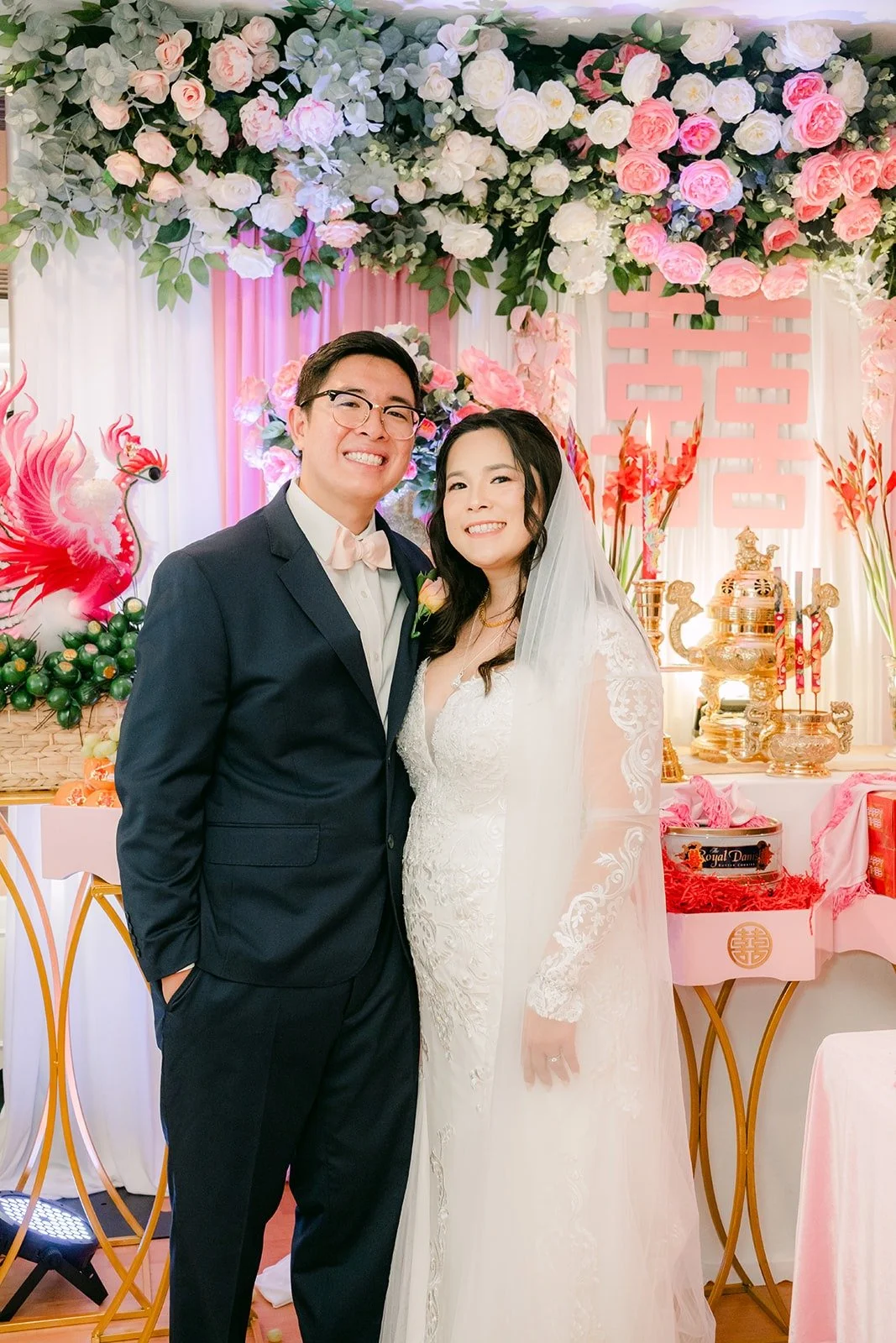 Amy and James smiling in front of the floral wall at home