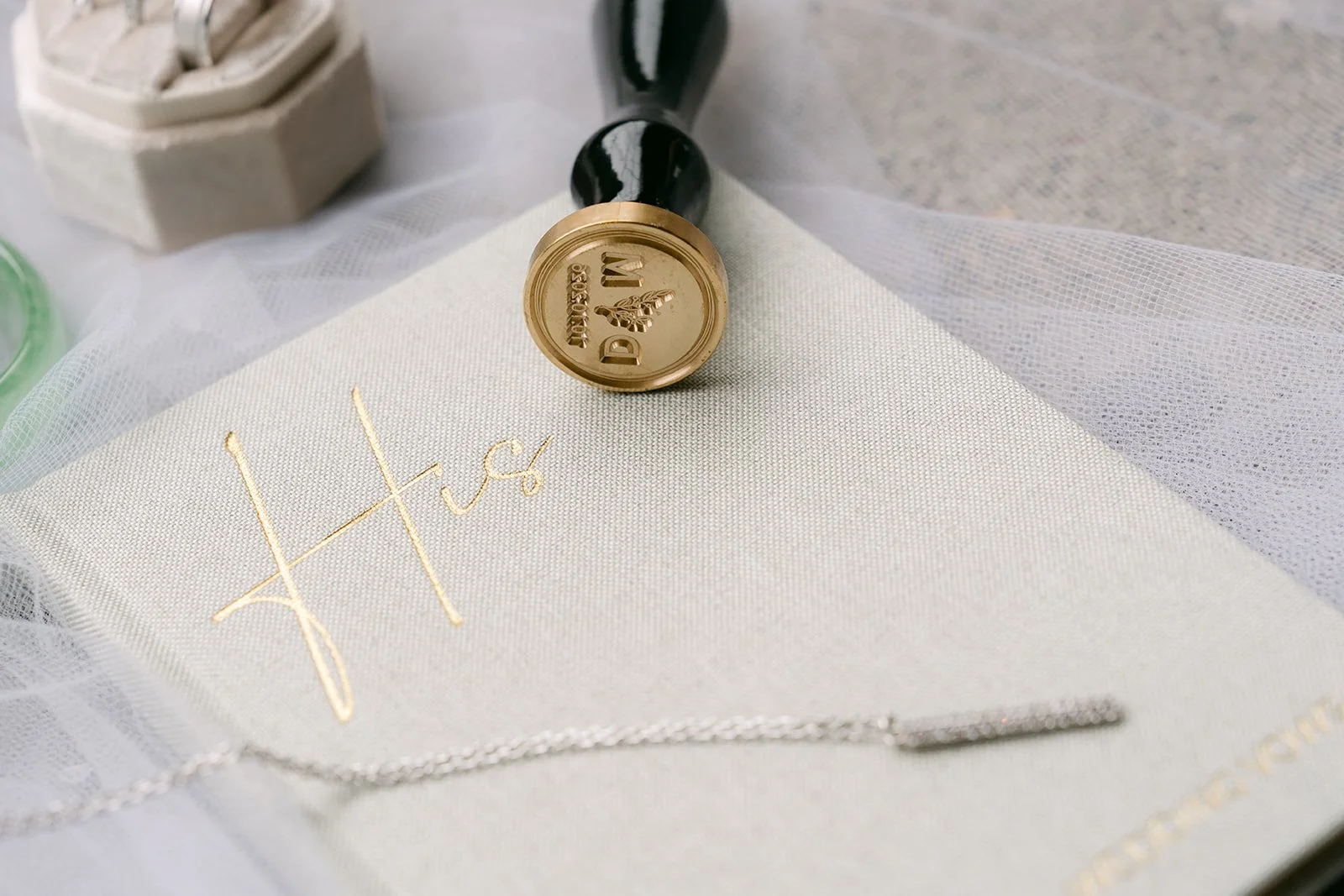 Gold wax seal stamp resting on a sage green vow book with gold lettering.