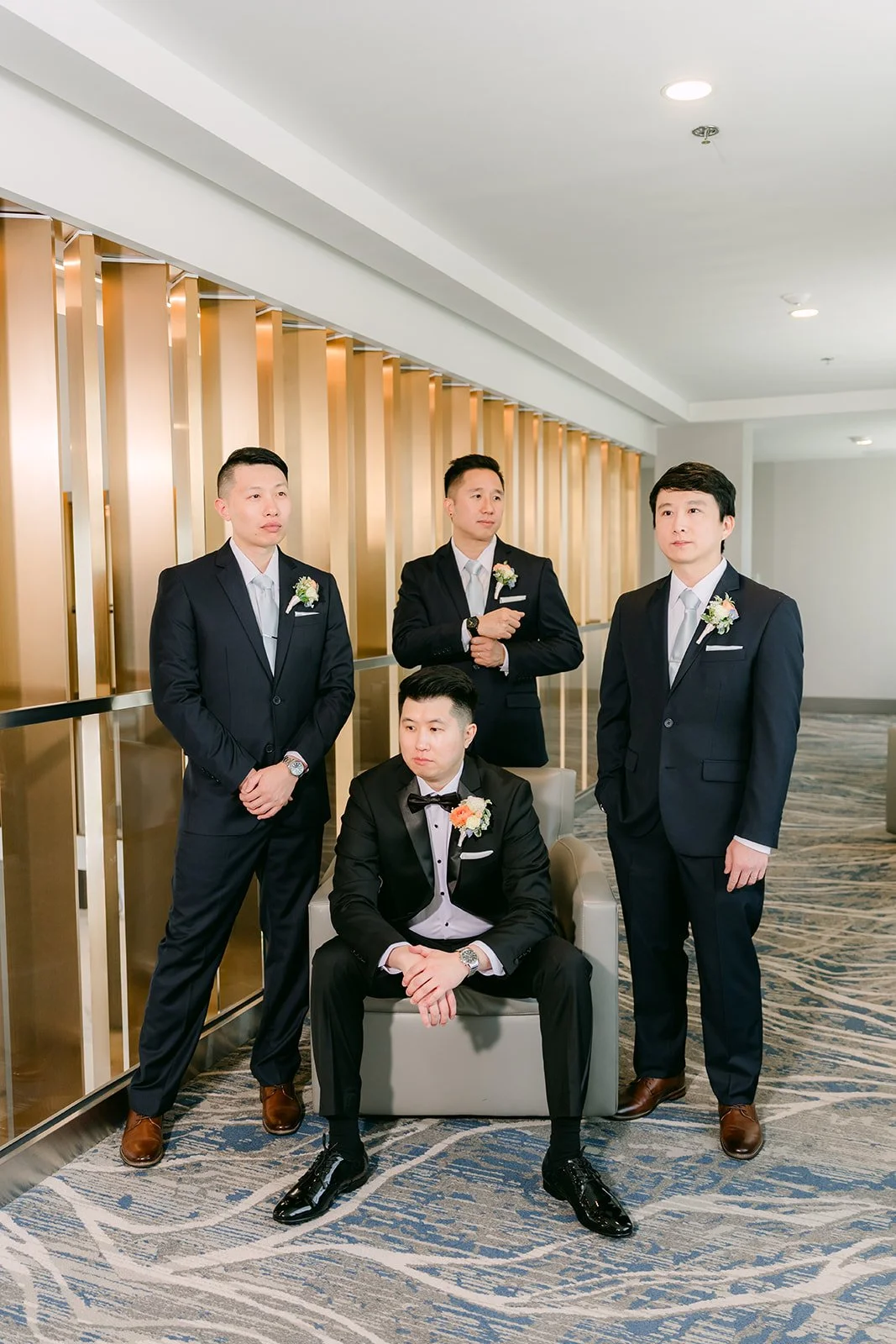 San and his groomsmen in black tuxedos by a gold wall.