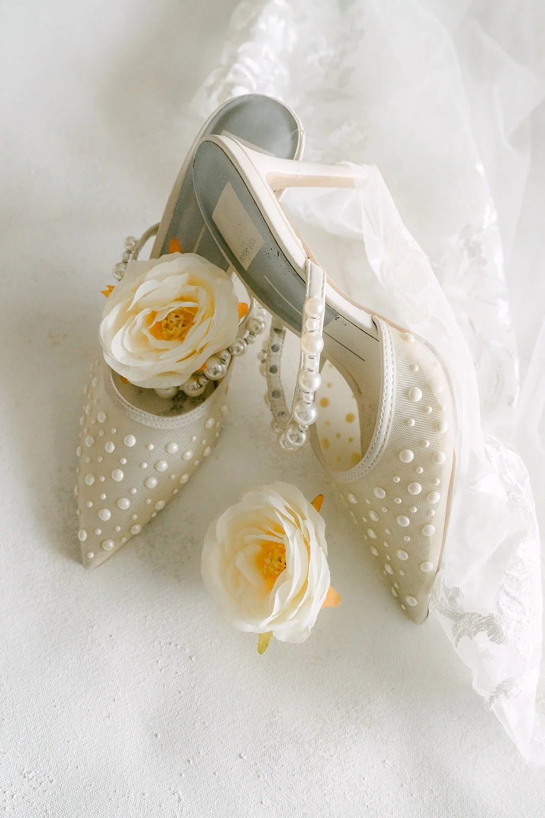 Jennifer's pearl detailed bridal heels beside white roses