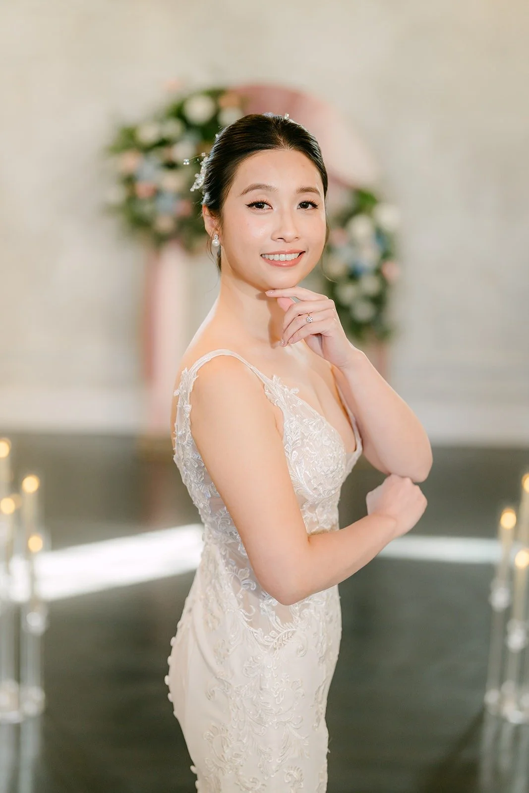 Elisa poses in her lace gown with her hand at her chin in the ceremony space