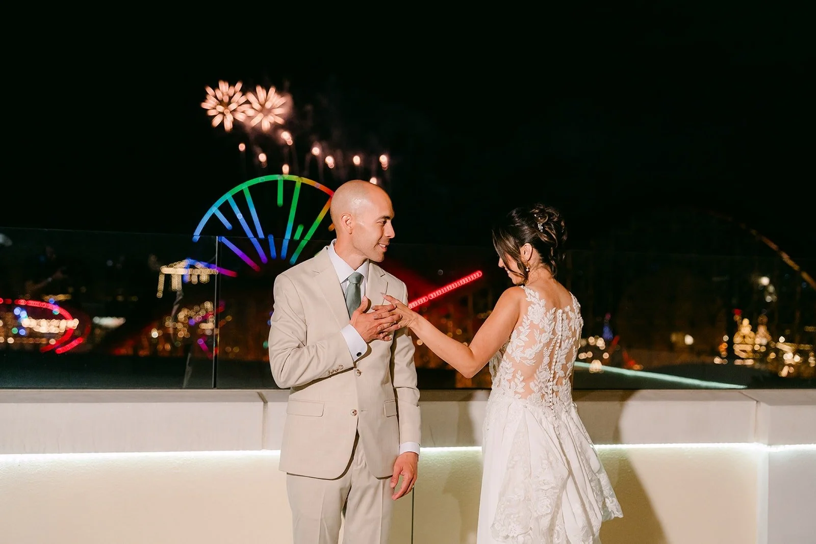 Francesca and Daniel face each other as fireworks burst over the theme park lights