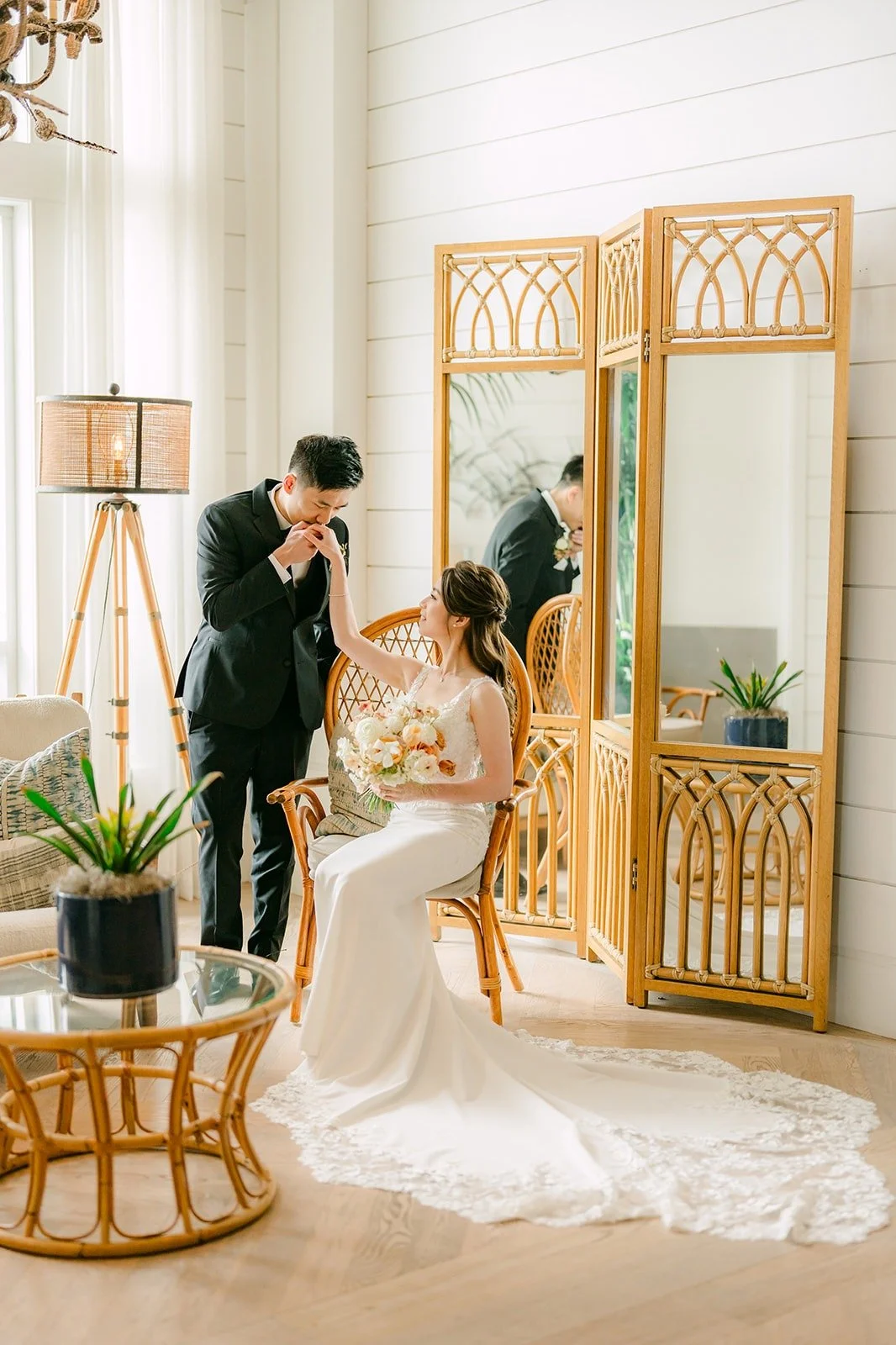 Angela and Eli beside a gold mirror and rattan chair in a sunlit lounge