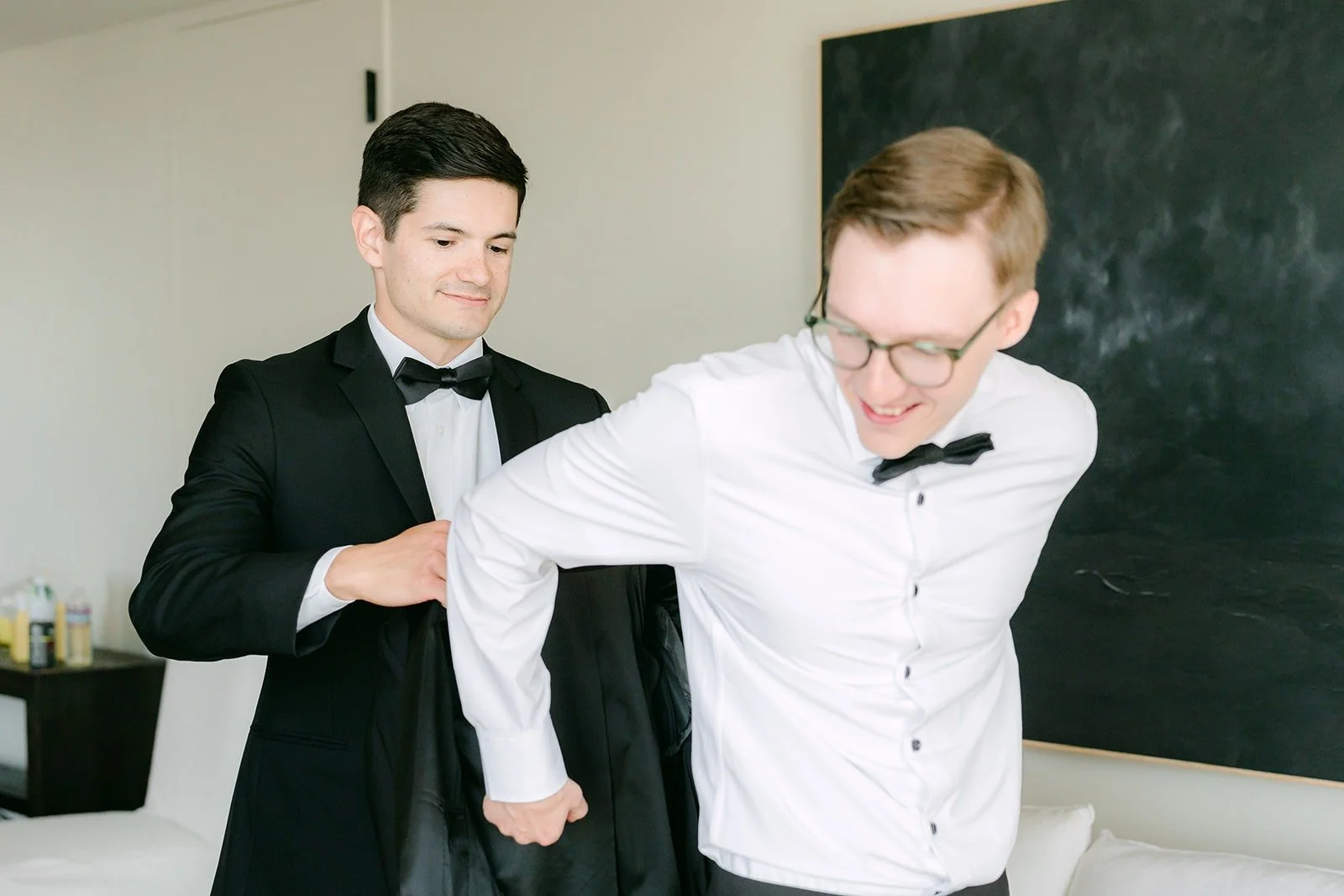 A groomsman helping Nik into his jacket