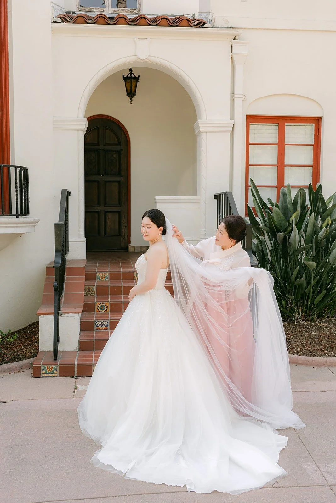 A family member adjusting Amy's veil outside the mansion