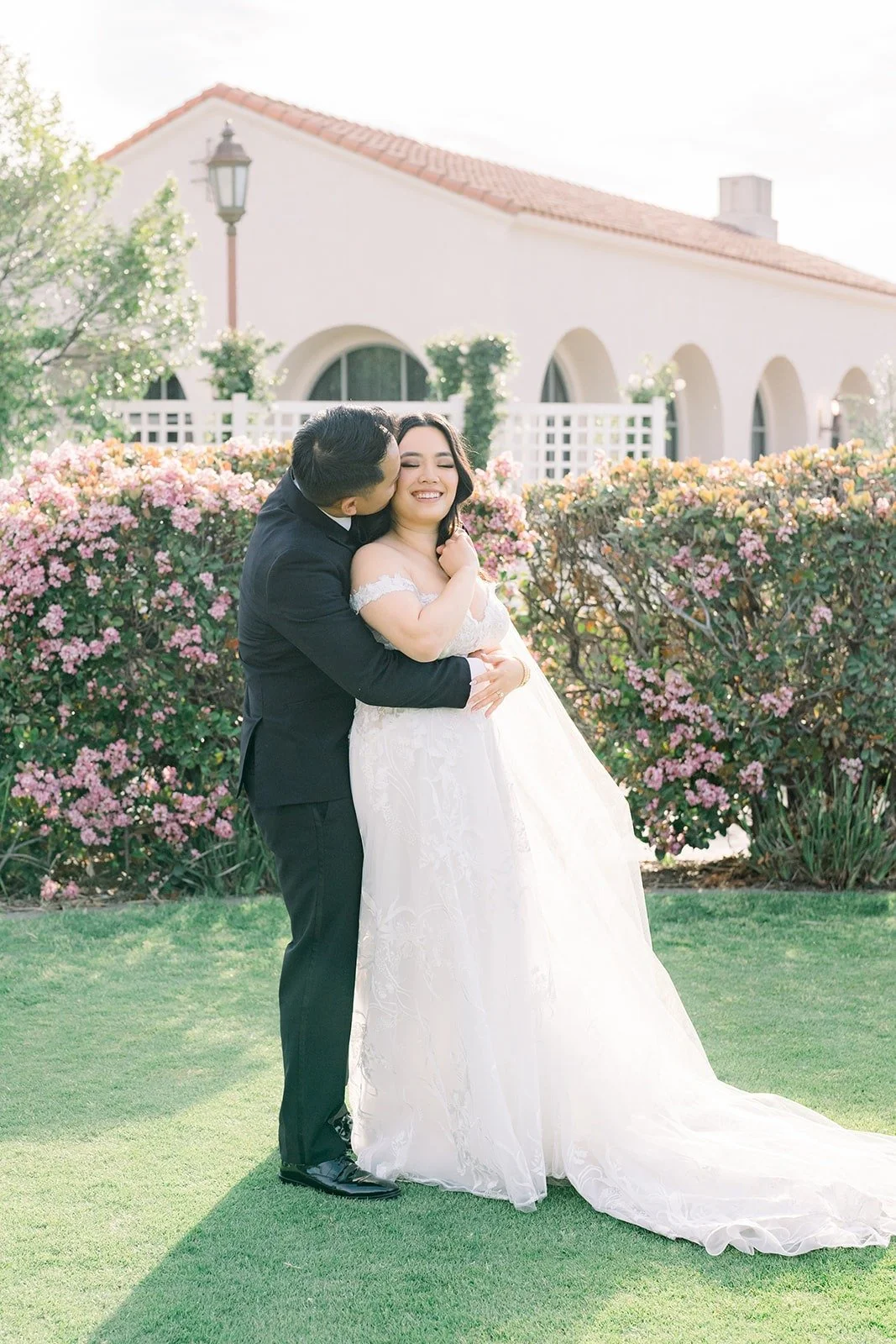Francesca and Ralph sharing a kiss beside the pink flowering hedges