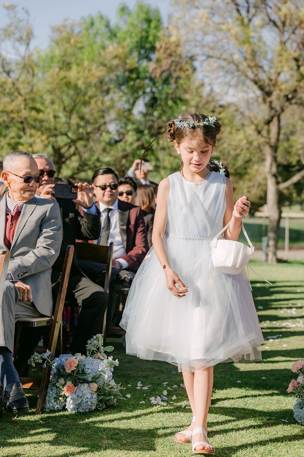 A flower girl in white walking down the aisle
