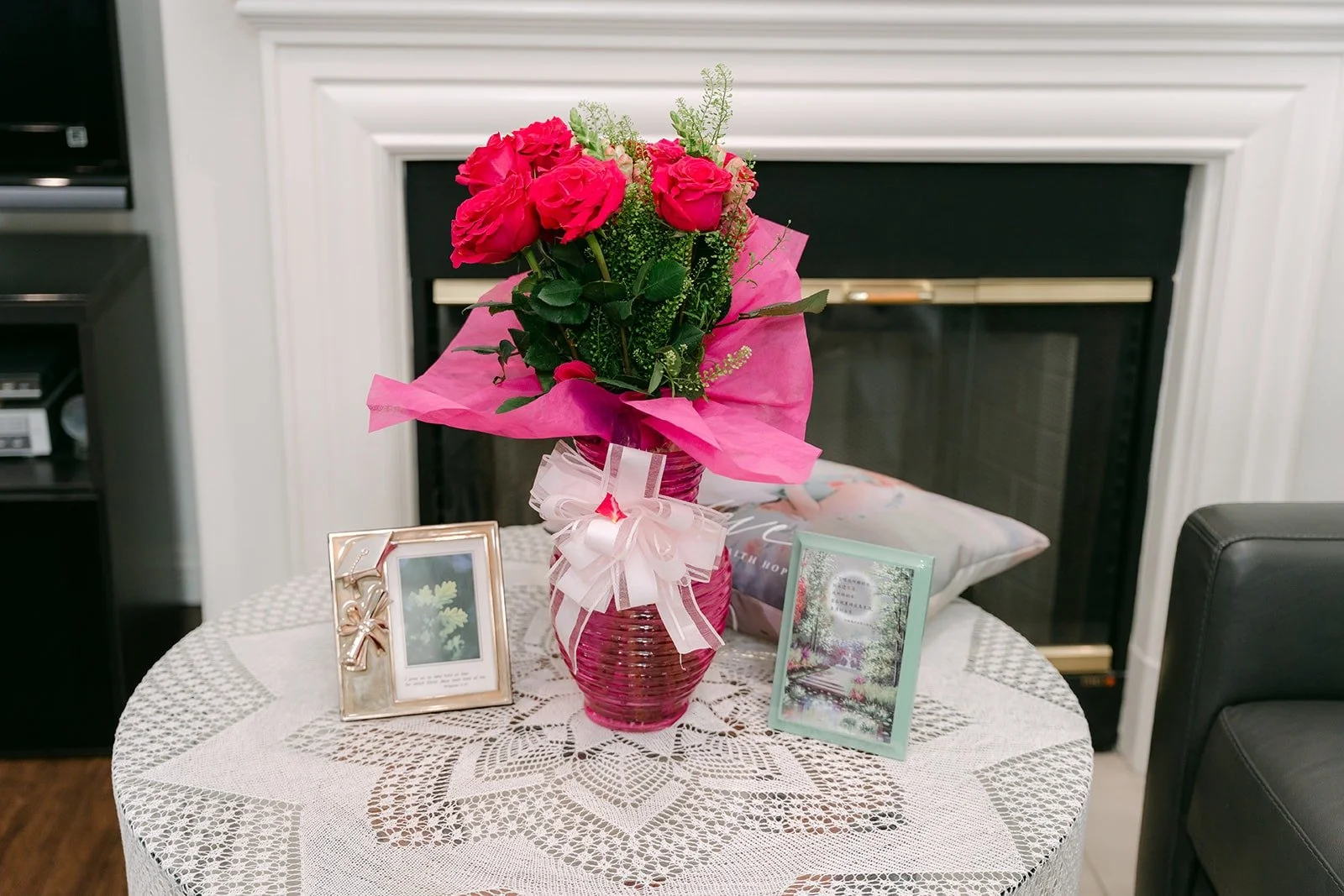 A bouquet of red roses and framed photos on a lace covered table in the living room