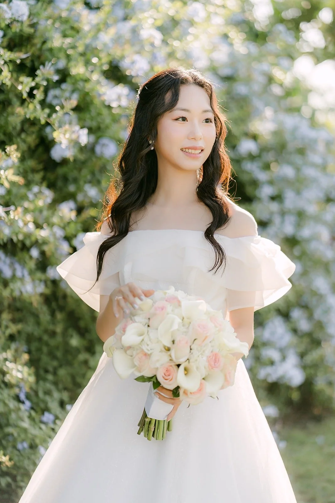 Jeannie holding her bouquet in front of blue flowering shrubs