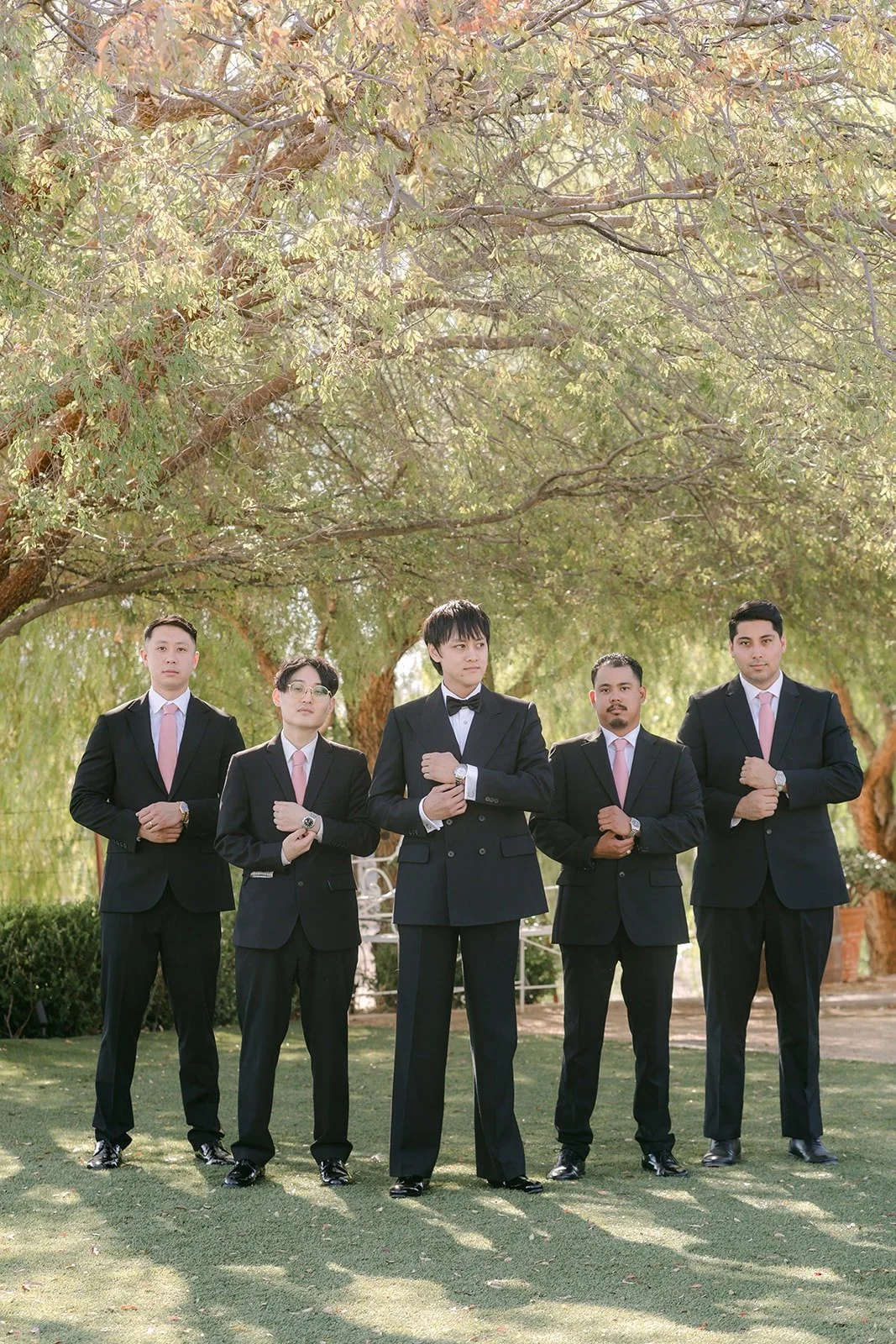 Job and his groomsmen in black tuxedos under the trees