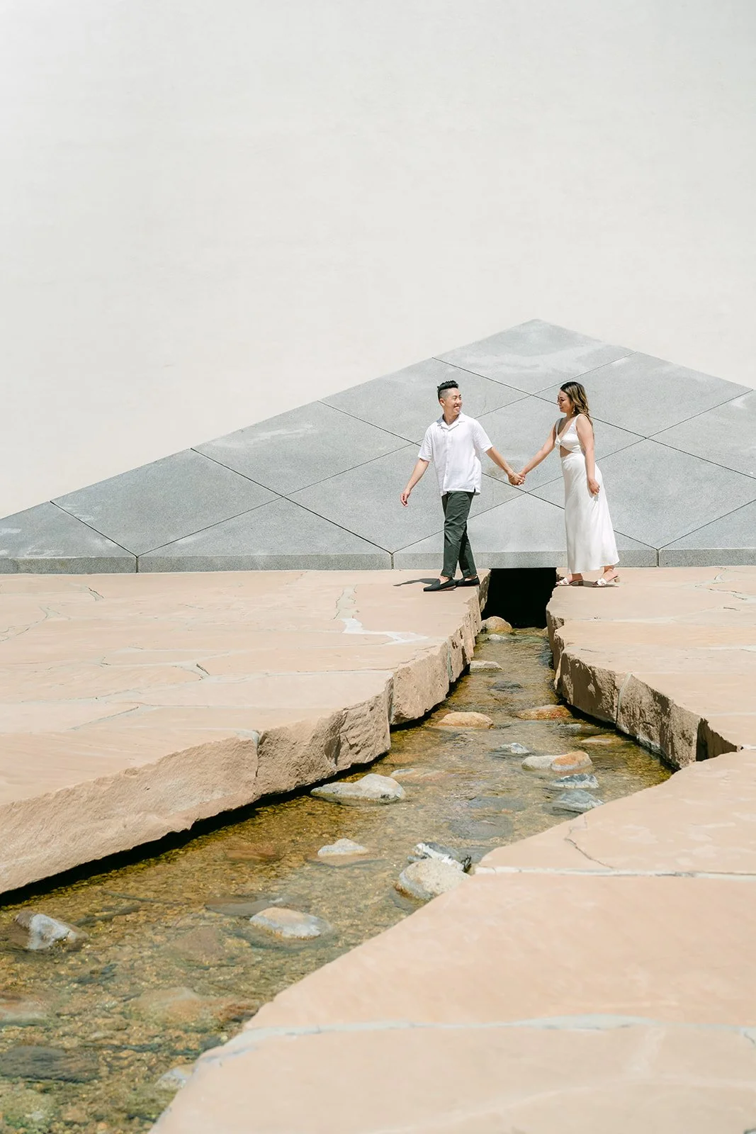 Stephanie and Alan holding hands by the stream with the pyramid behind them.