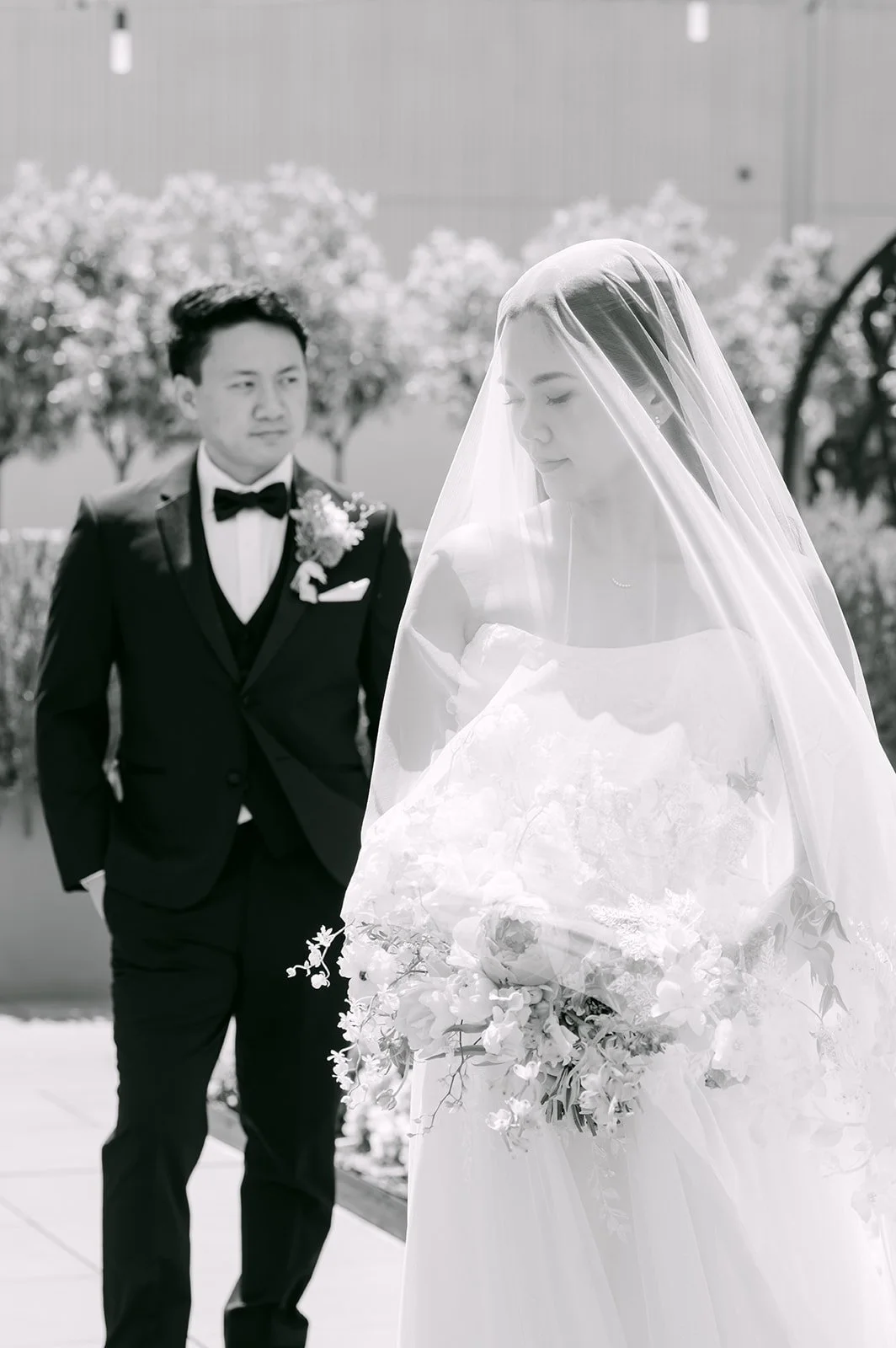 Black and white portrait of the groom watching his bride under her veil