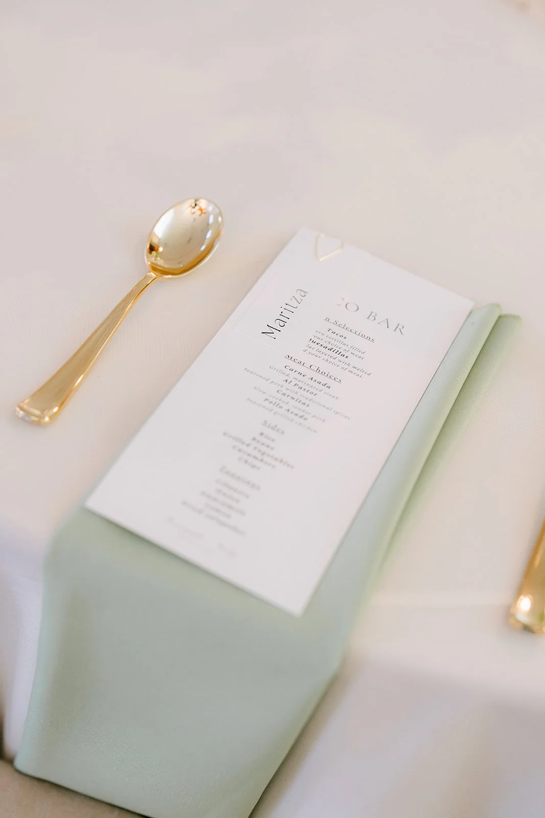 A place card and gold flatware on a sage napkin.