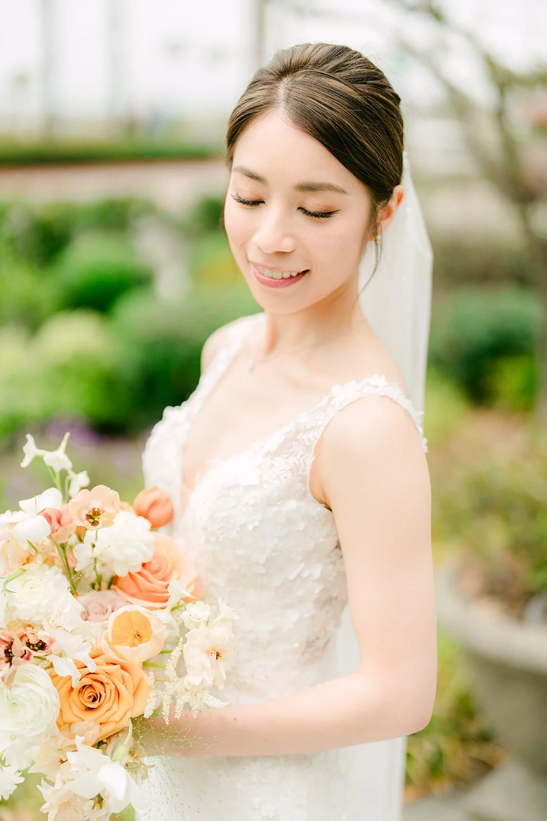 Angela smiling down at her bouquet, her veil soft behind her, photographed by One and Only Production
