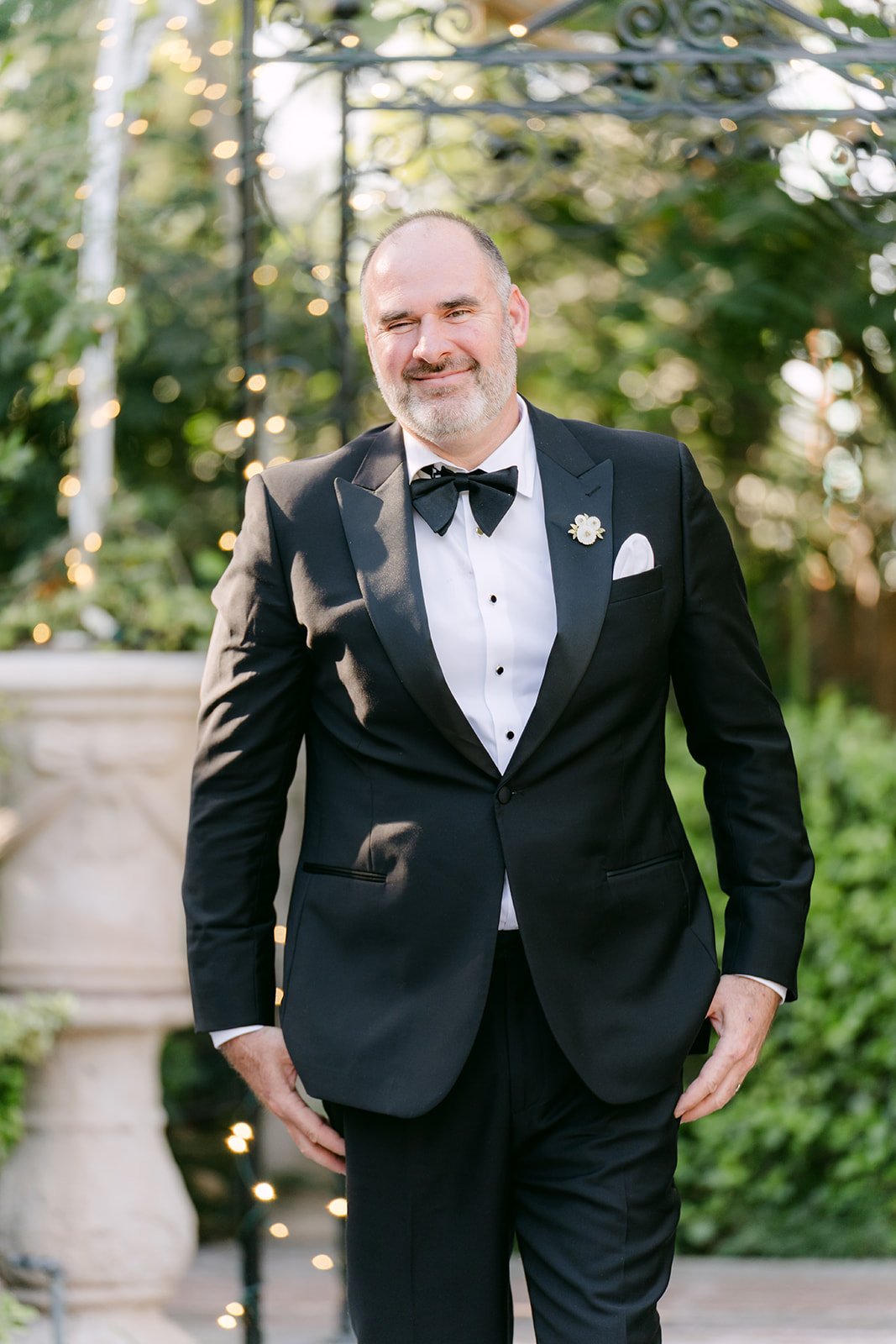 A guest in a black tuxedo smiling as he walks down the aisle.