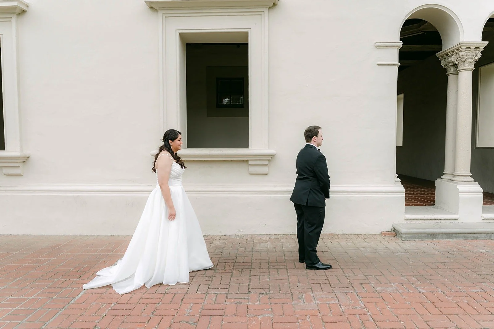 Saira walking up behind Matthew for their first look in an Athenaeum courtyard