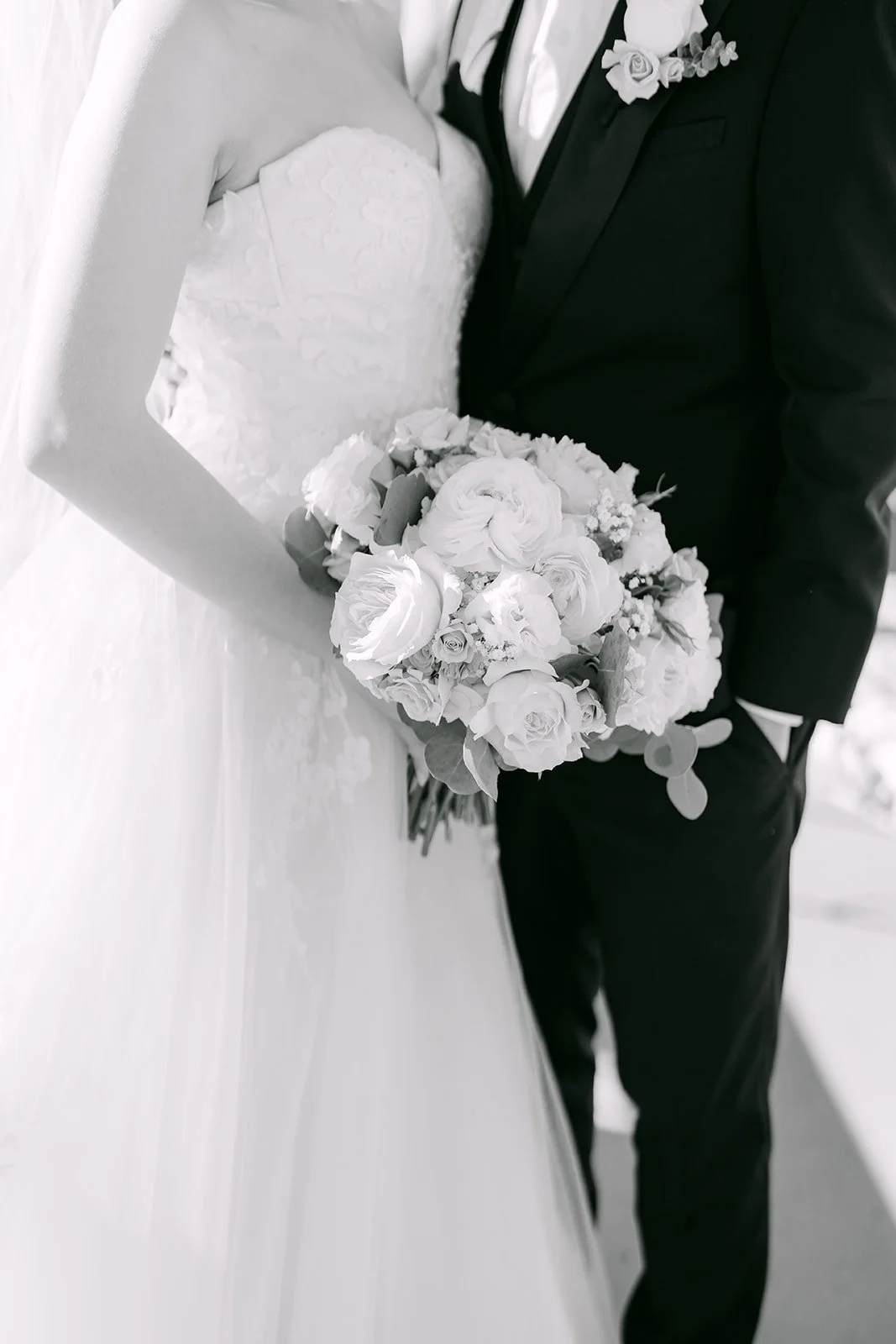 Black and white detail of the bride's bouquet and the groom's tuxedo