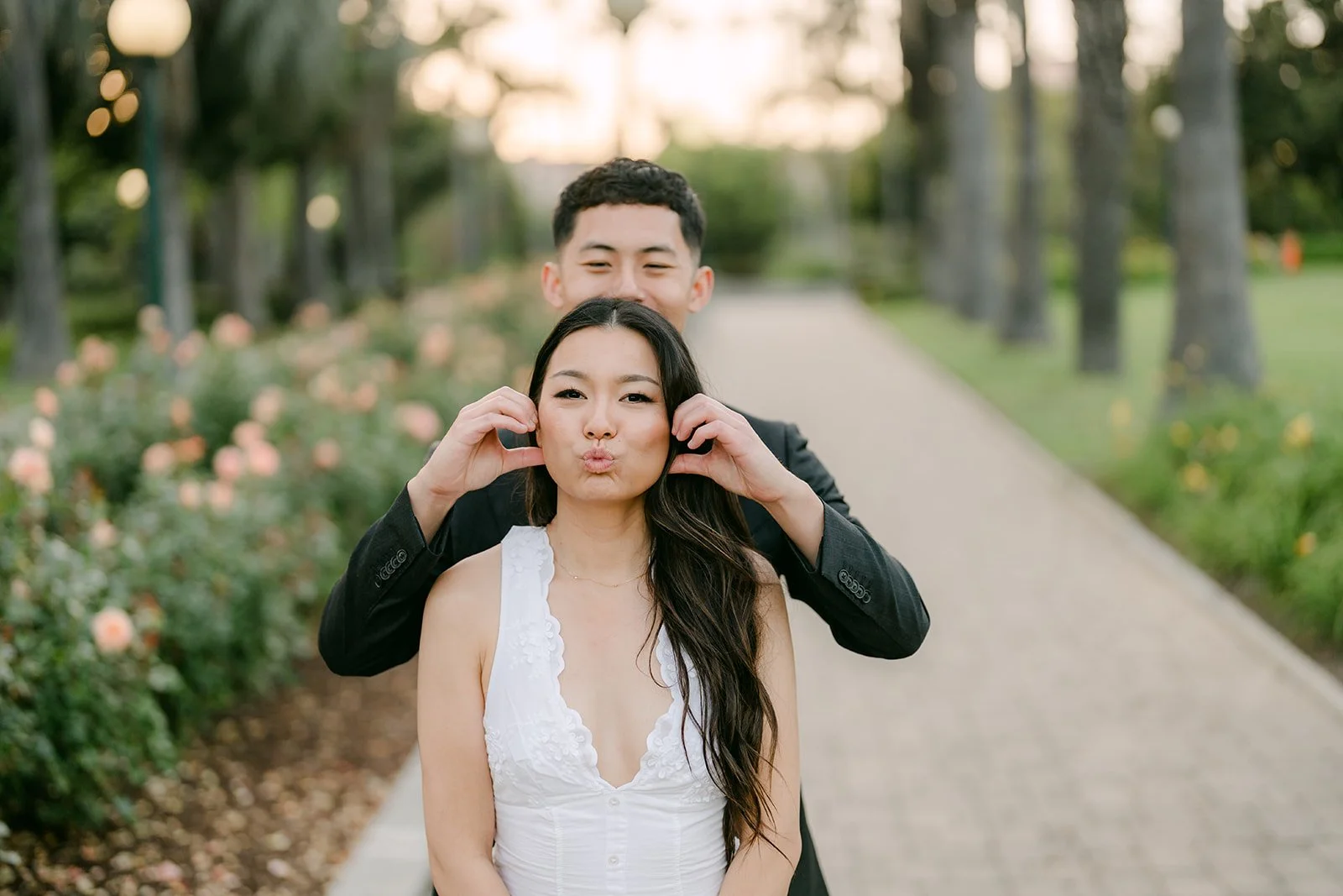 Jadee laughs while Richard stands behind her on the rose garden path, photographed by One and Only Production.