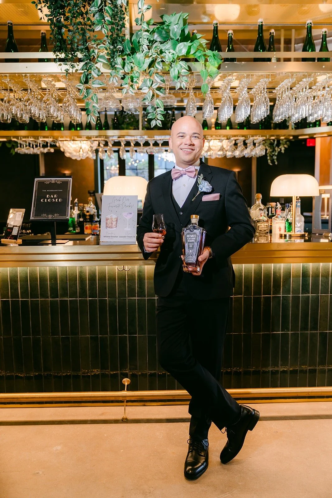 Brandon in his black tuxedo standing in front of the bar at The Headquarters