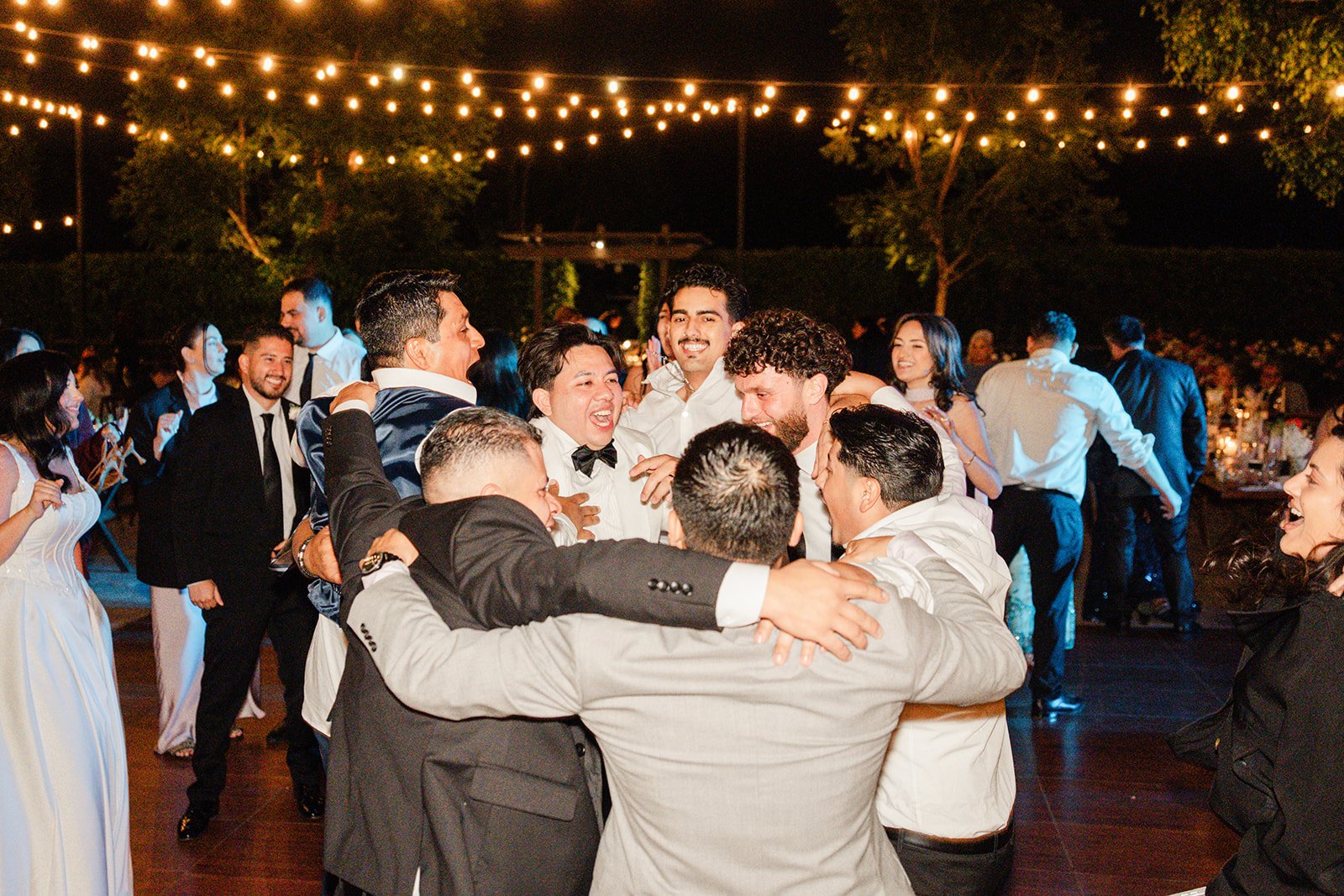 Groomsmen celebrating on the dance floor under string lights