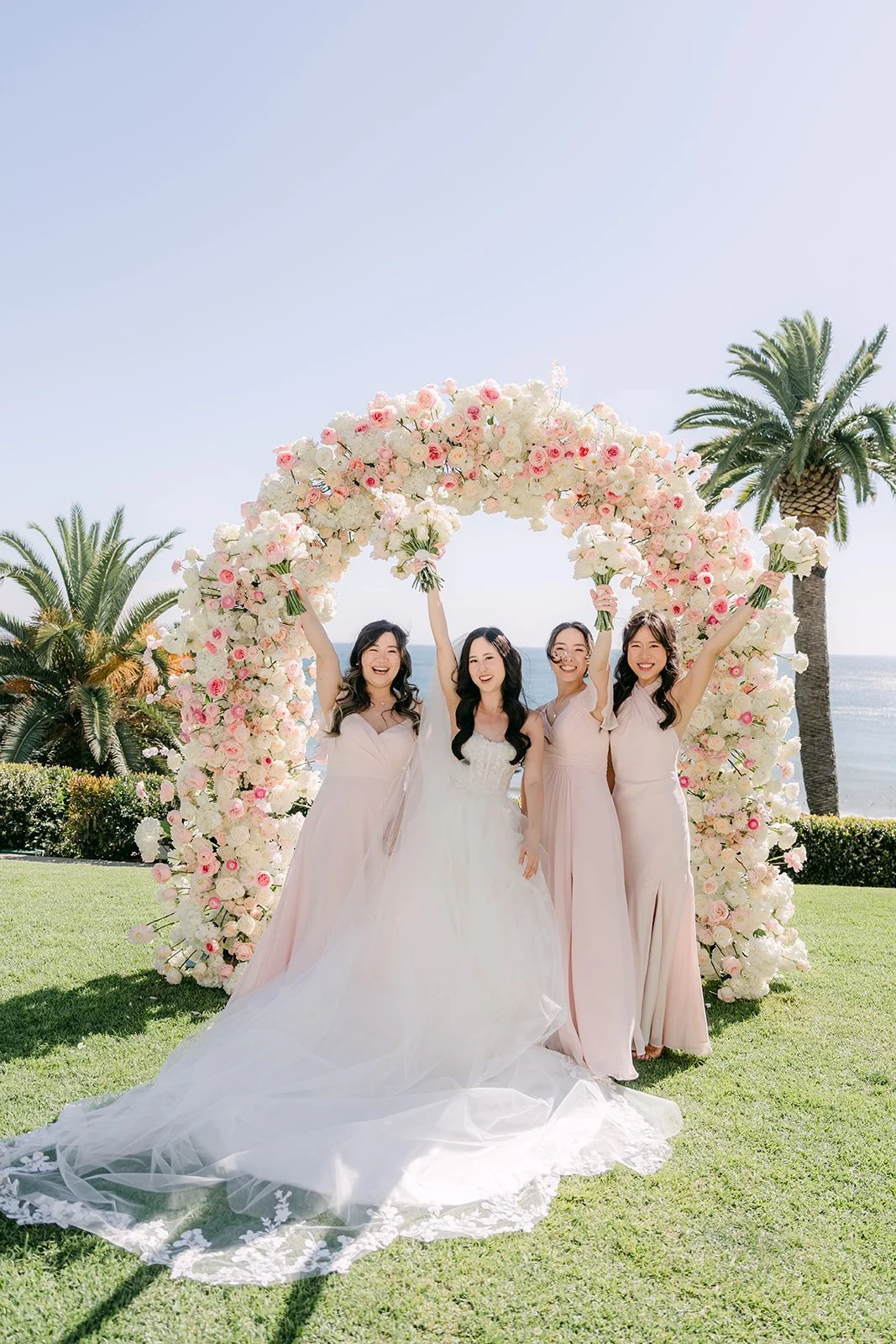 Bride and bridesmaids in blush dresses in front of the ceremony arch