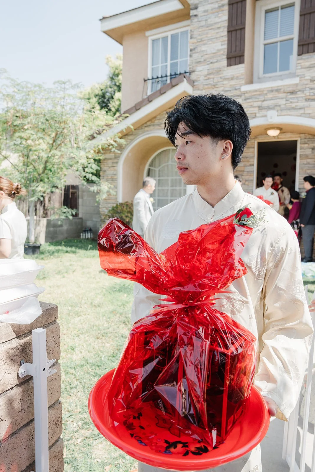 A groomsman carrying a red wrapped gift tray.