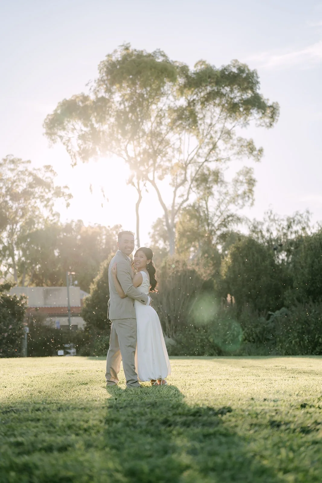 Kim and Vincent embracing on the meadow as the sun lowers behind the trees.